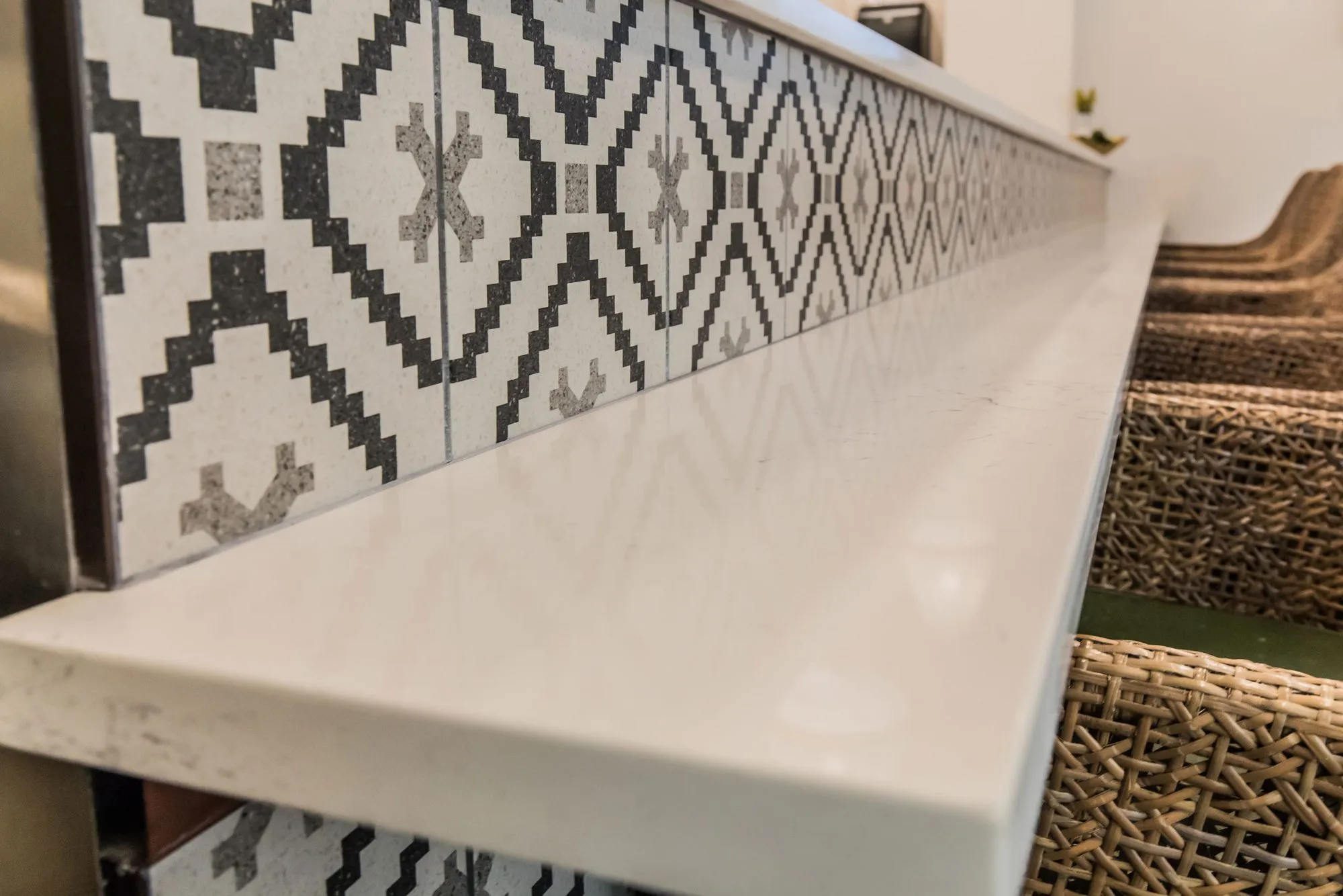 Senior living bistro counter, a white quartz edge above black and white geometric tile, woven chair backs at right
