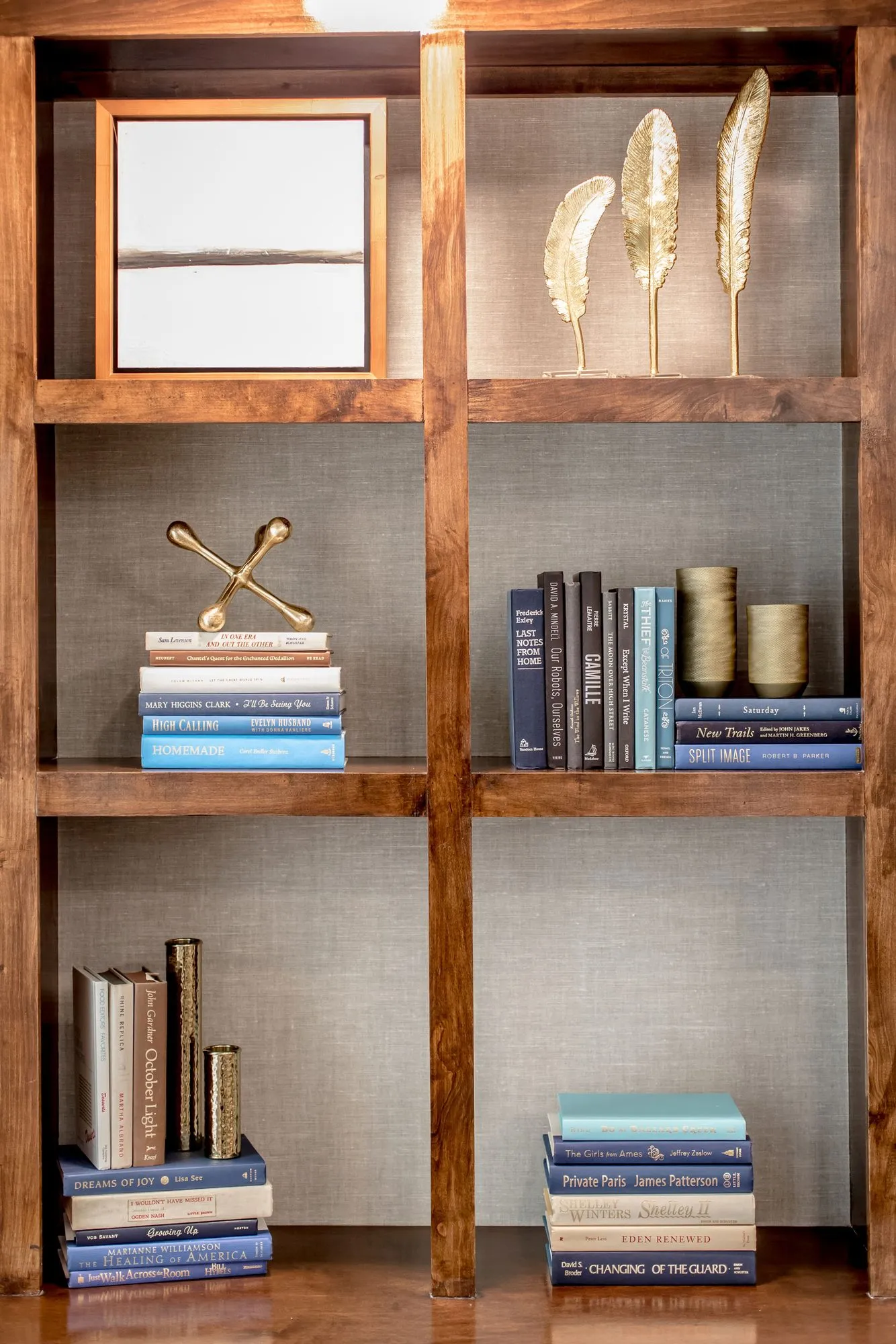Senior living interior detail: wood bookcase styled with blue books, gold feather sculptures, a brass jack and a framed print