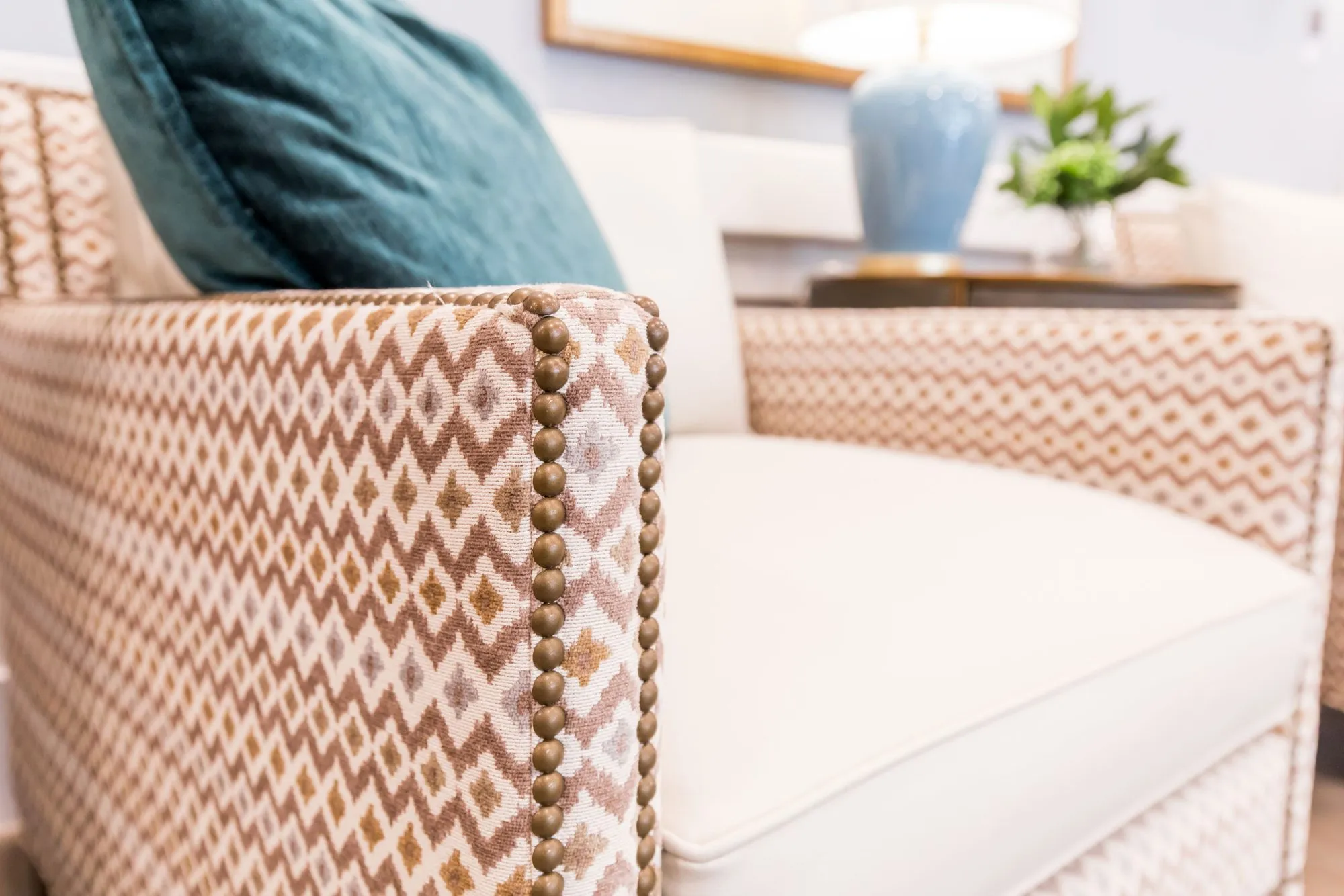 Senior living interior detail: sofa arm in rust and cream diamond upholstery with brass nailheads, a teal pillow above