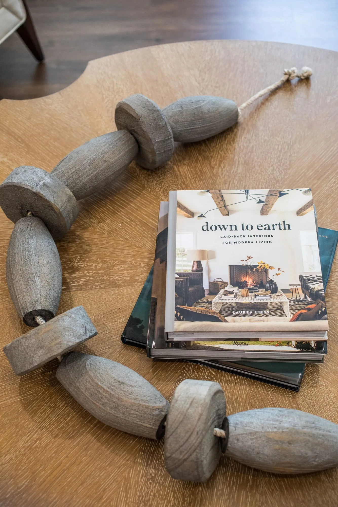 Senior living interior detail: round wood coffee table with a stack of design books beside a carved wood bead garland