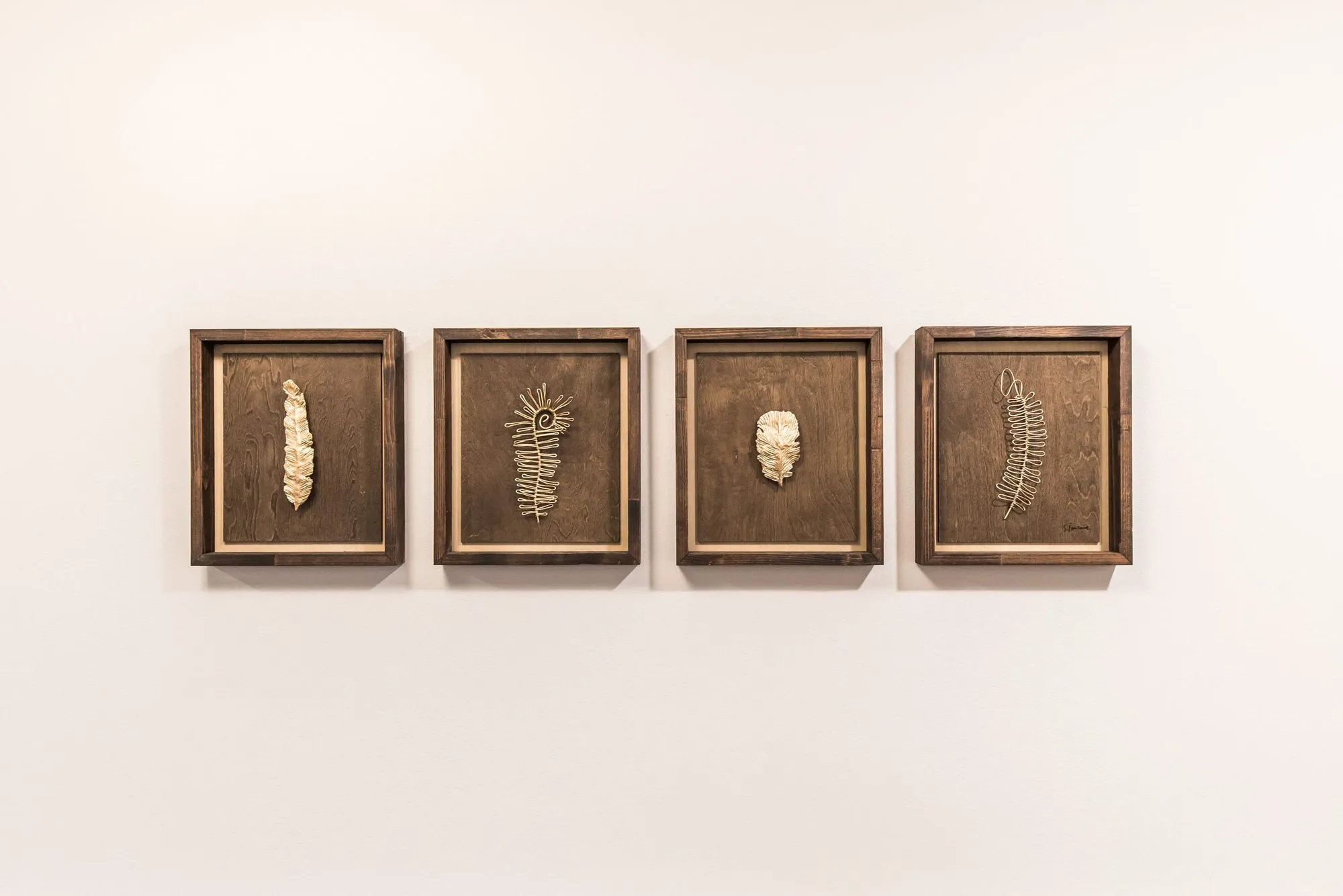 Senior living interior detail: four wood shadow box frames holding gilded leaf and fern forms on a white wall