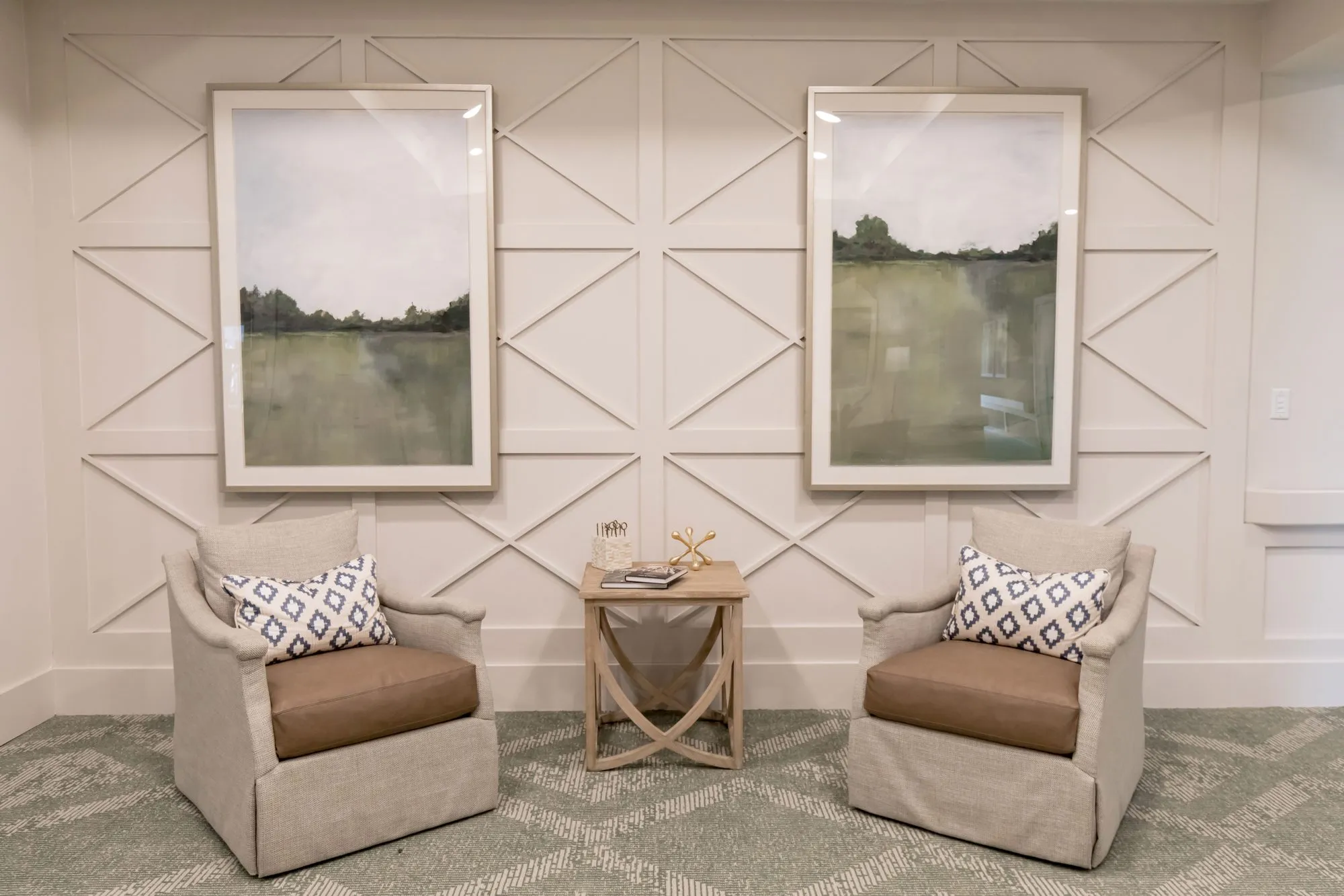 Senior living interior detail: two linen skirted armchairs with leather seats below green landscape prints on a panelled wall