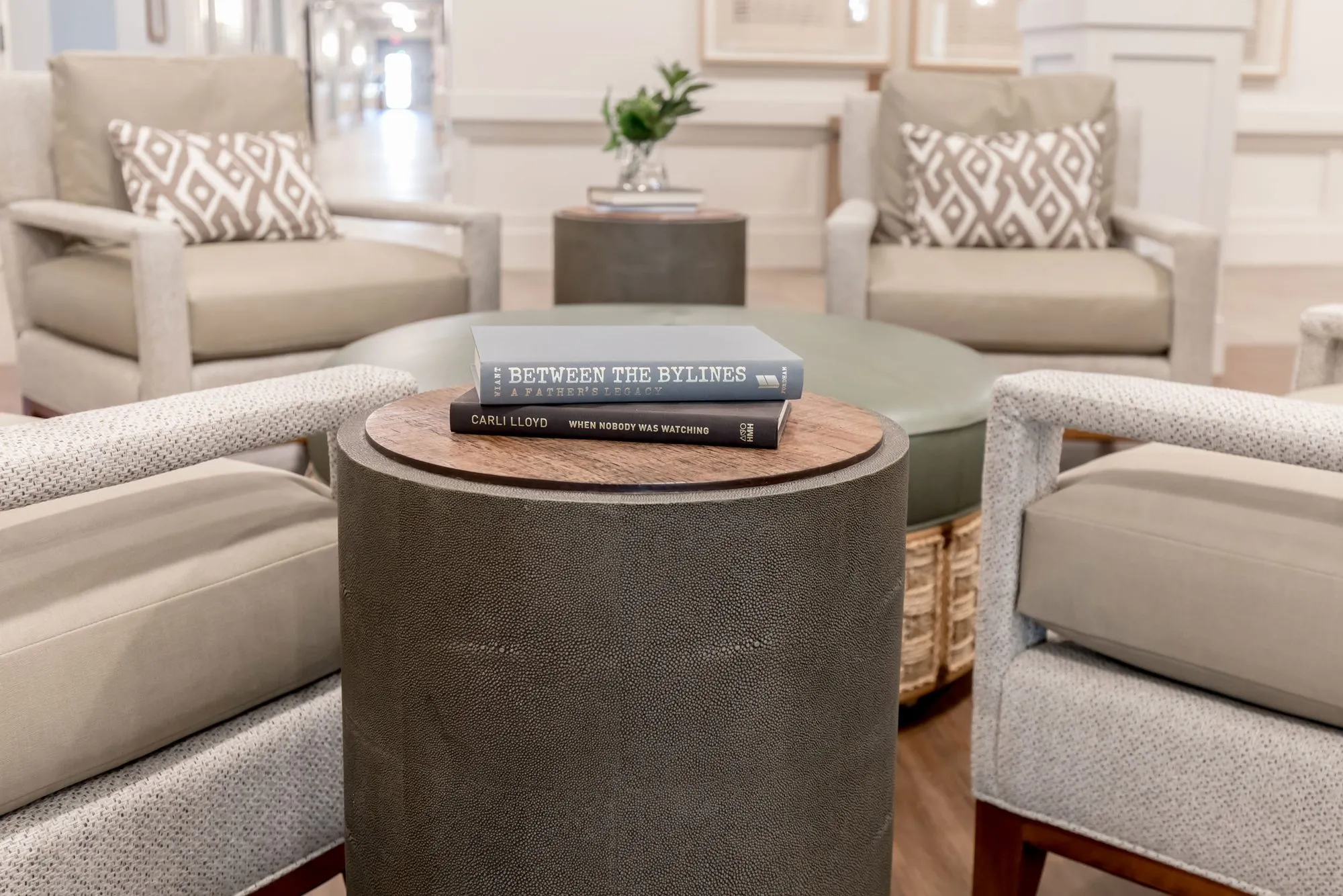 Senior living interior detail: shagreen drum table with books among linen armchairs and diamond pattern pillows