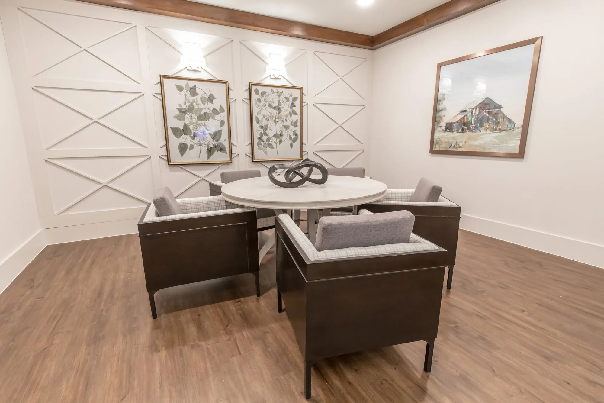 Senior living private dining room with grey upholstered chairs at a round table, botanical prints and a barn painting