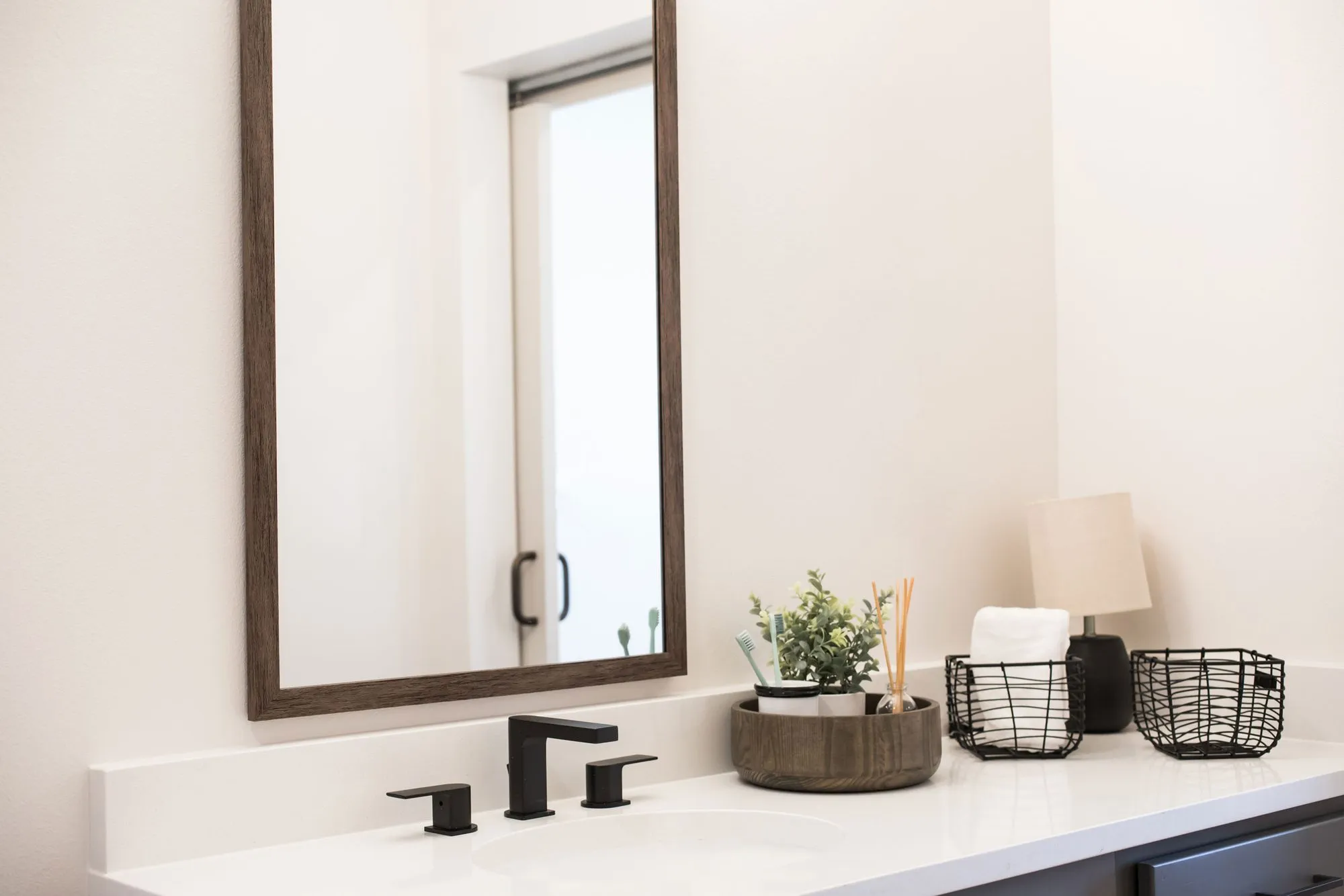 Senior living bathroom vanity with a black faucet, wood-framed mirror and wire baskets of toiletries