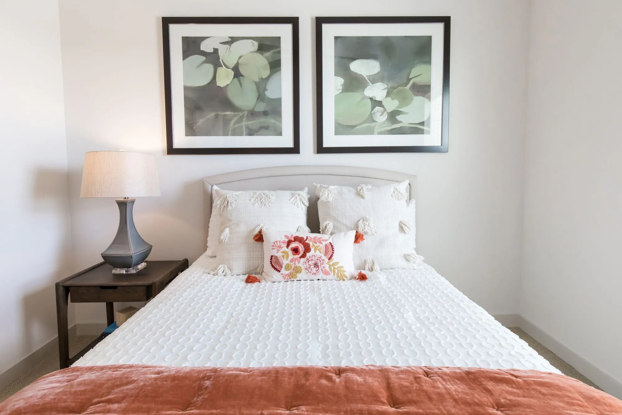 Senior living bedroom with an upholstered arched headboard, white tufted pillows and a rust coverlet below lily pad prints