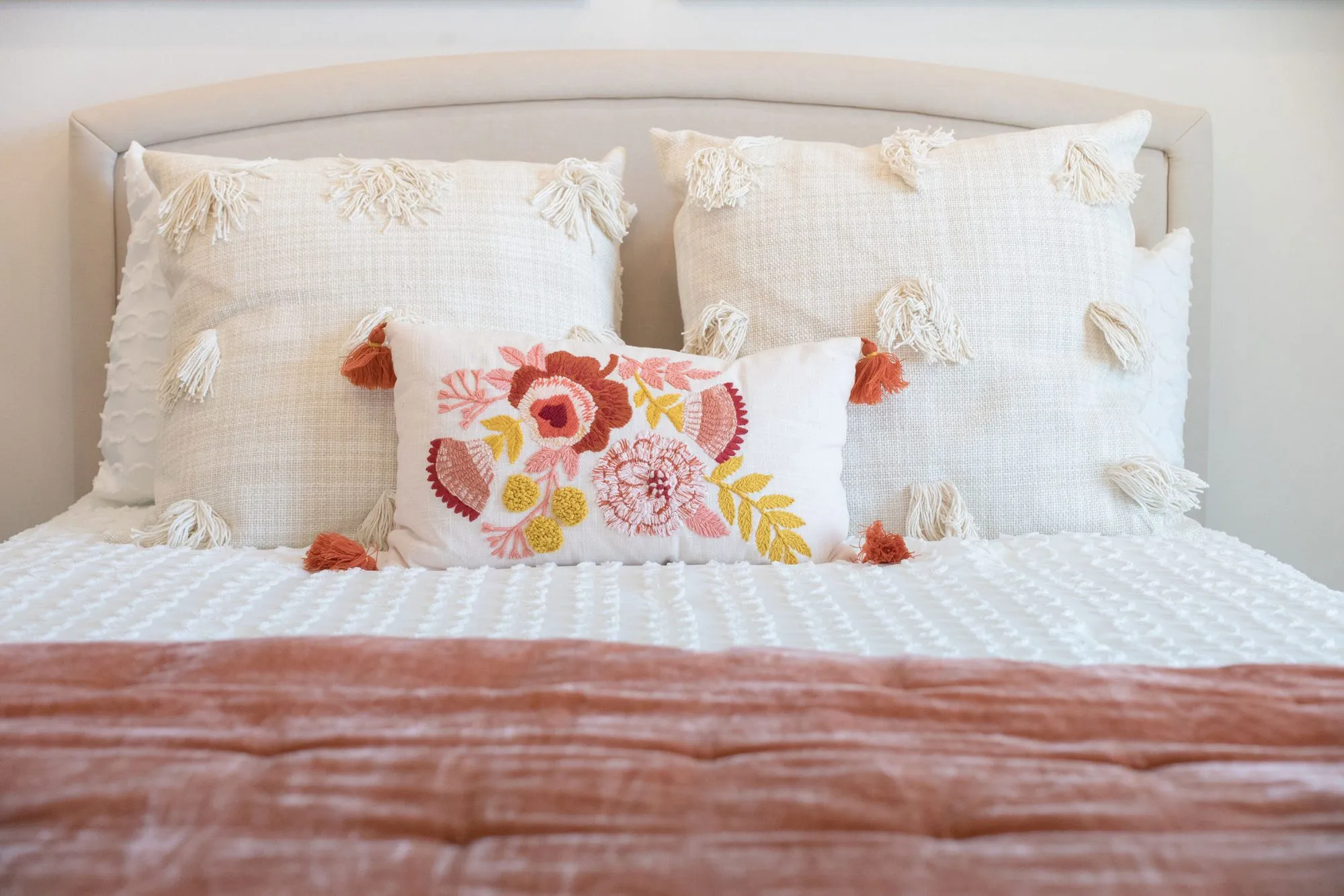 Senior living interior detail: white tasselled pillows and a floral embroidered cushion on a bed with a rust throw