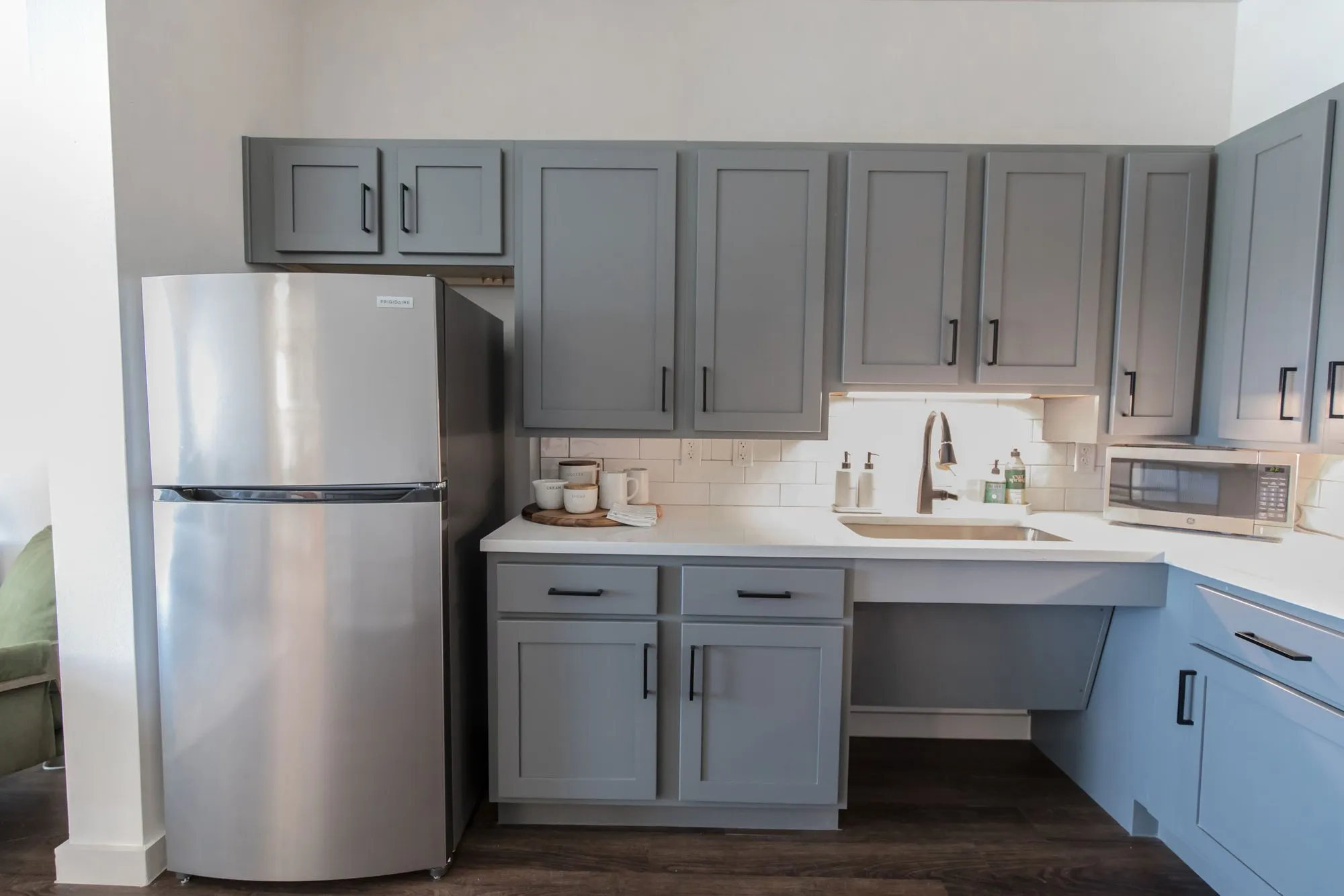 Senior living apartment kitchenette with grey shaker cabinets, a stainless refrigerator and a lowered accessible sink