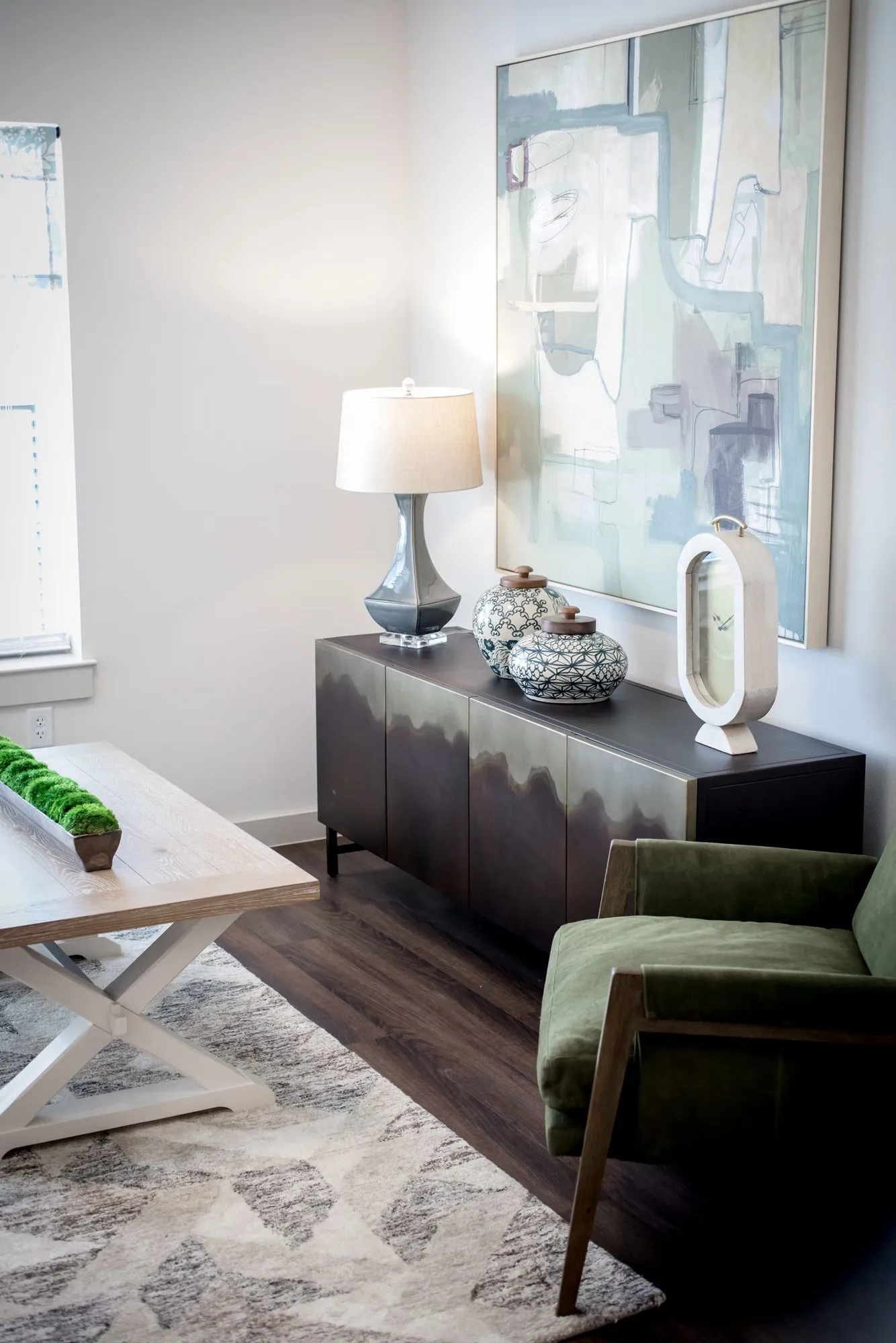 Senior living interior detail: olive velvet armchair beside a dark sideboard with a lamp and blue ginger jars