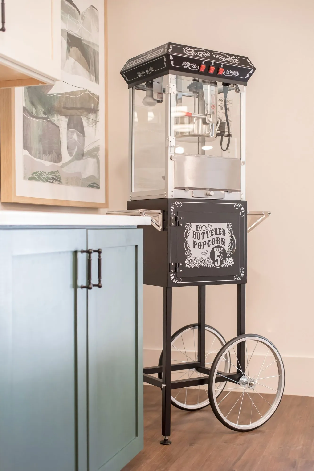 Senior living interior detail: vintage-style popcorn cart beside teal cabinetry in front of a framed print