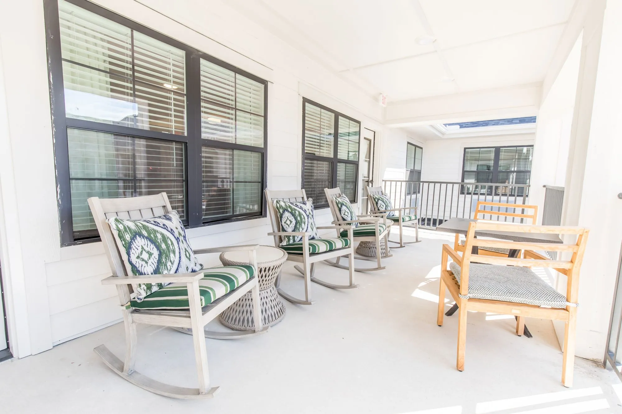 Senior living covered porch with white rockers and green striped cushions toward a wood dining set