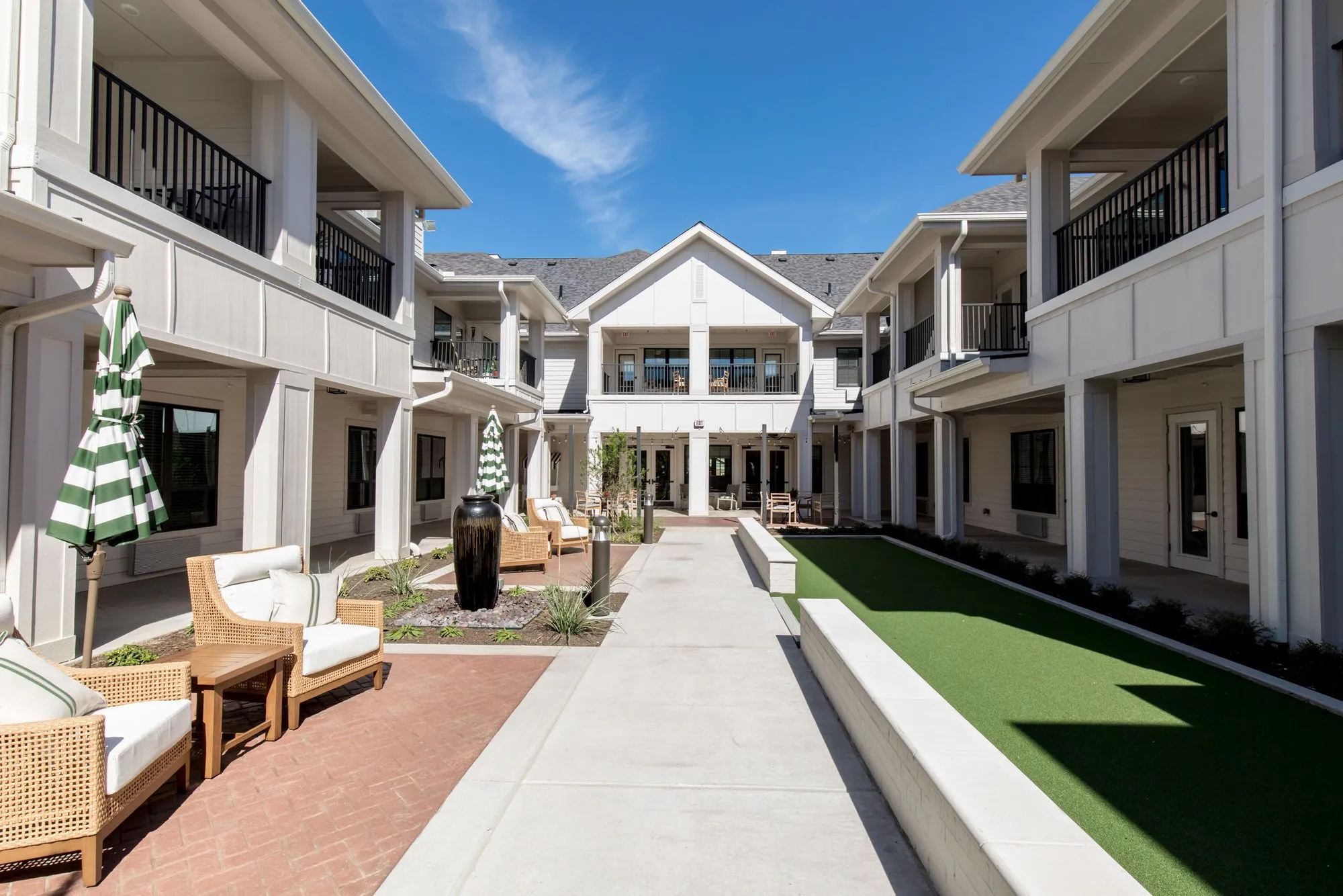 Senior living courtyard between two storey white wings, green striped umbrellas, rattan chairs and a turf lawn