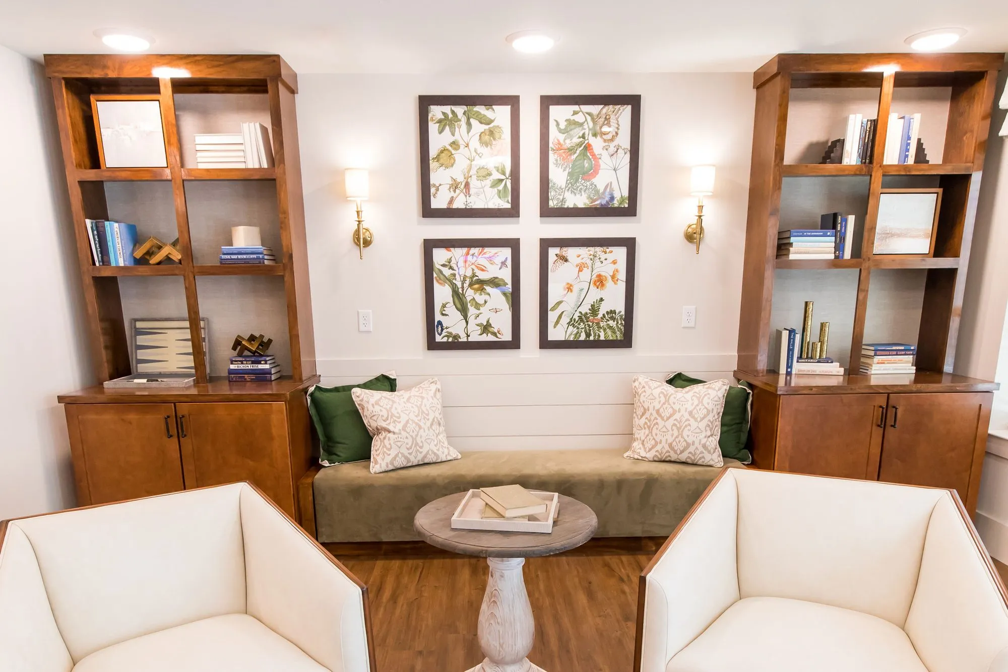 Senior living library nook with a green banquette between wood bookcases, botanical prints and two white armchairs