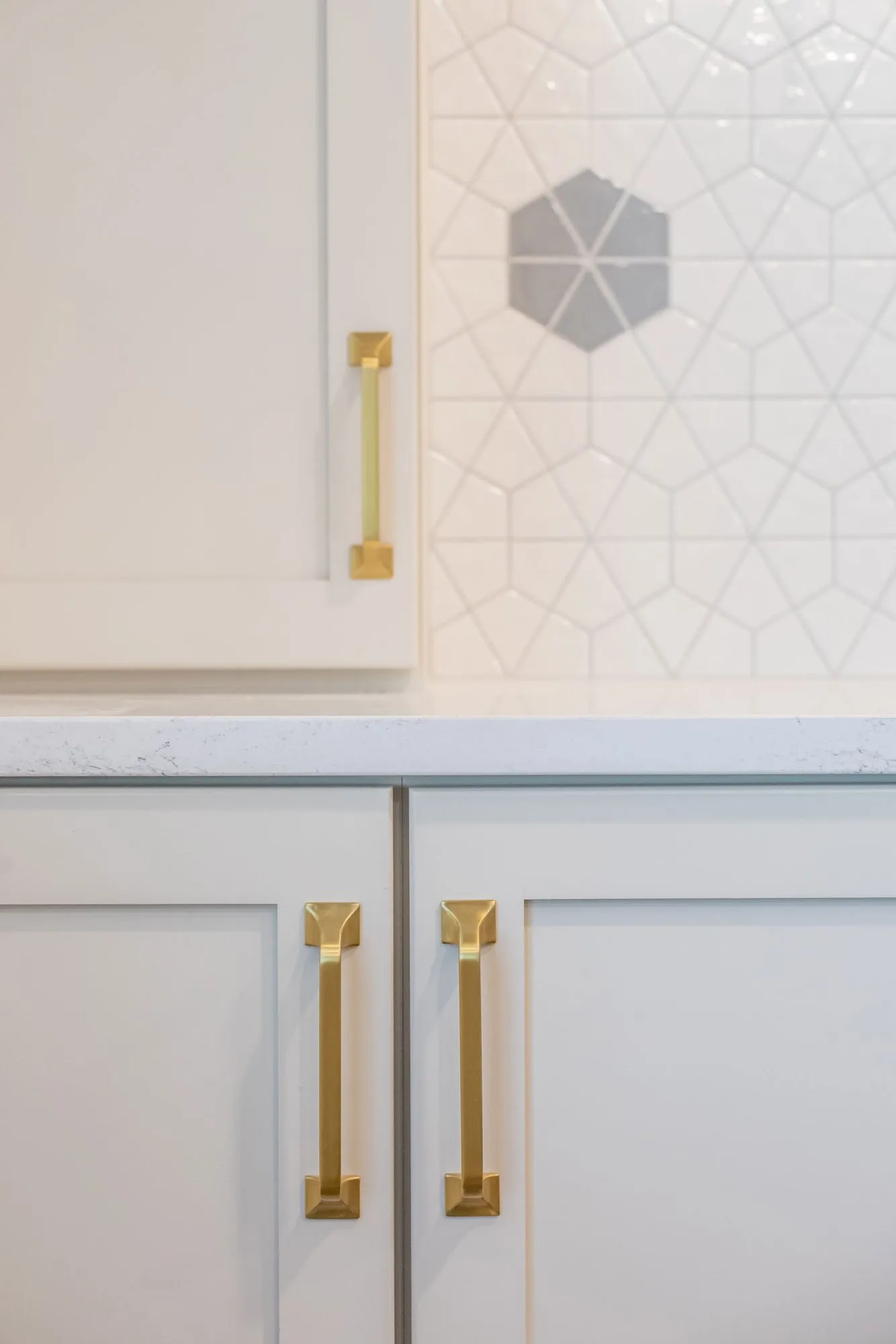 Senior living interior detail: white shaker cabinets with brass pulls against white geometric tile with grey hexagon accents
