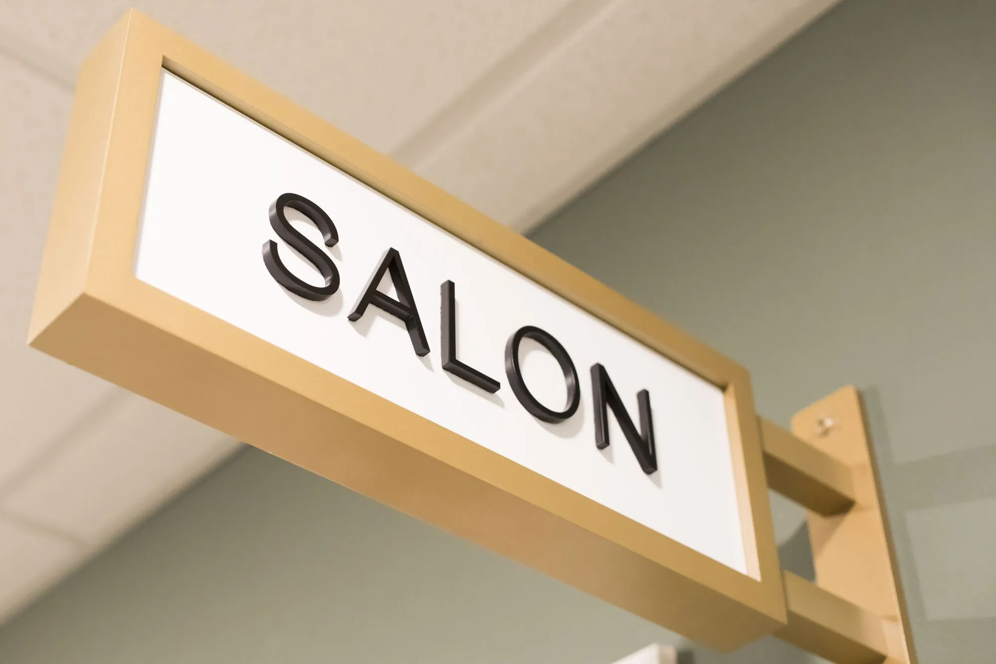Senior living interior detail: brass projecting room sign reading Salon
