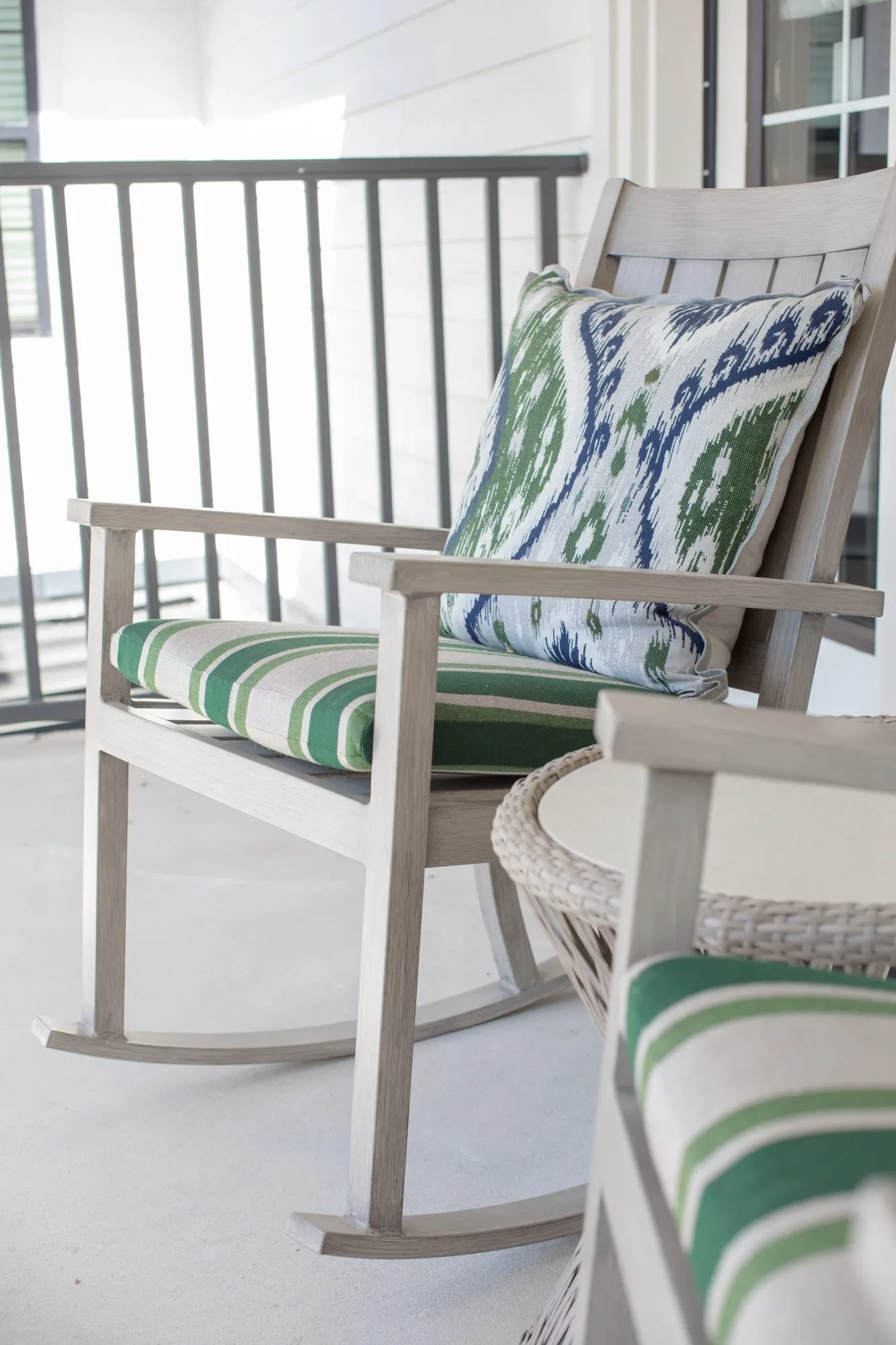Senior living covered porch with a grey wood rocking chair, green striped cushion and ikat pillow by the railing