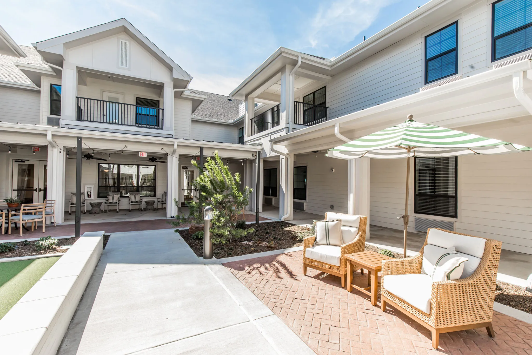 Senior living courtyard with a striped umbrella over rattan seating on brick paving below the resident balconies