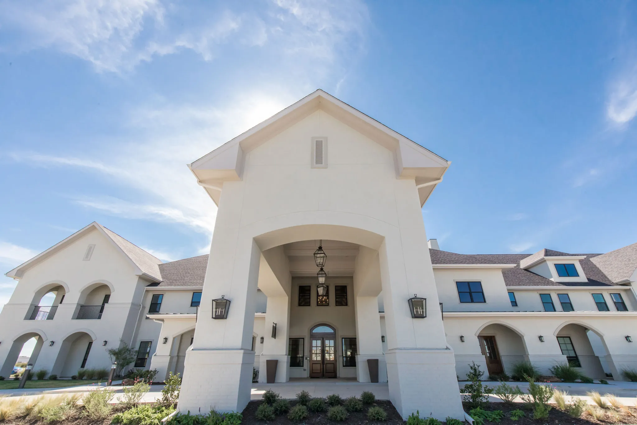 Senior living community exterior: white stucco gable and arched porte cochere above the arrival doors