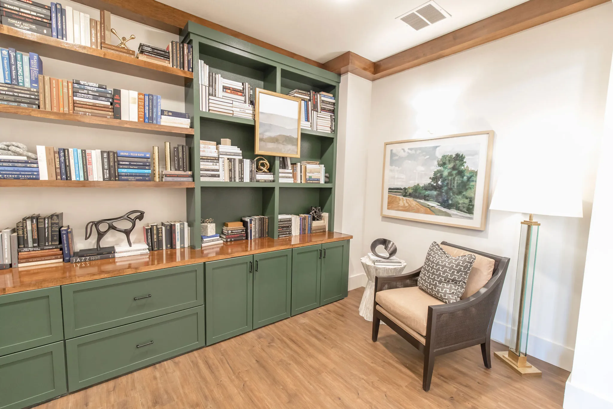 Senior living library with sage built-ins filled with books and a bronze horse beside a cane-back reading chair