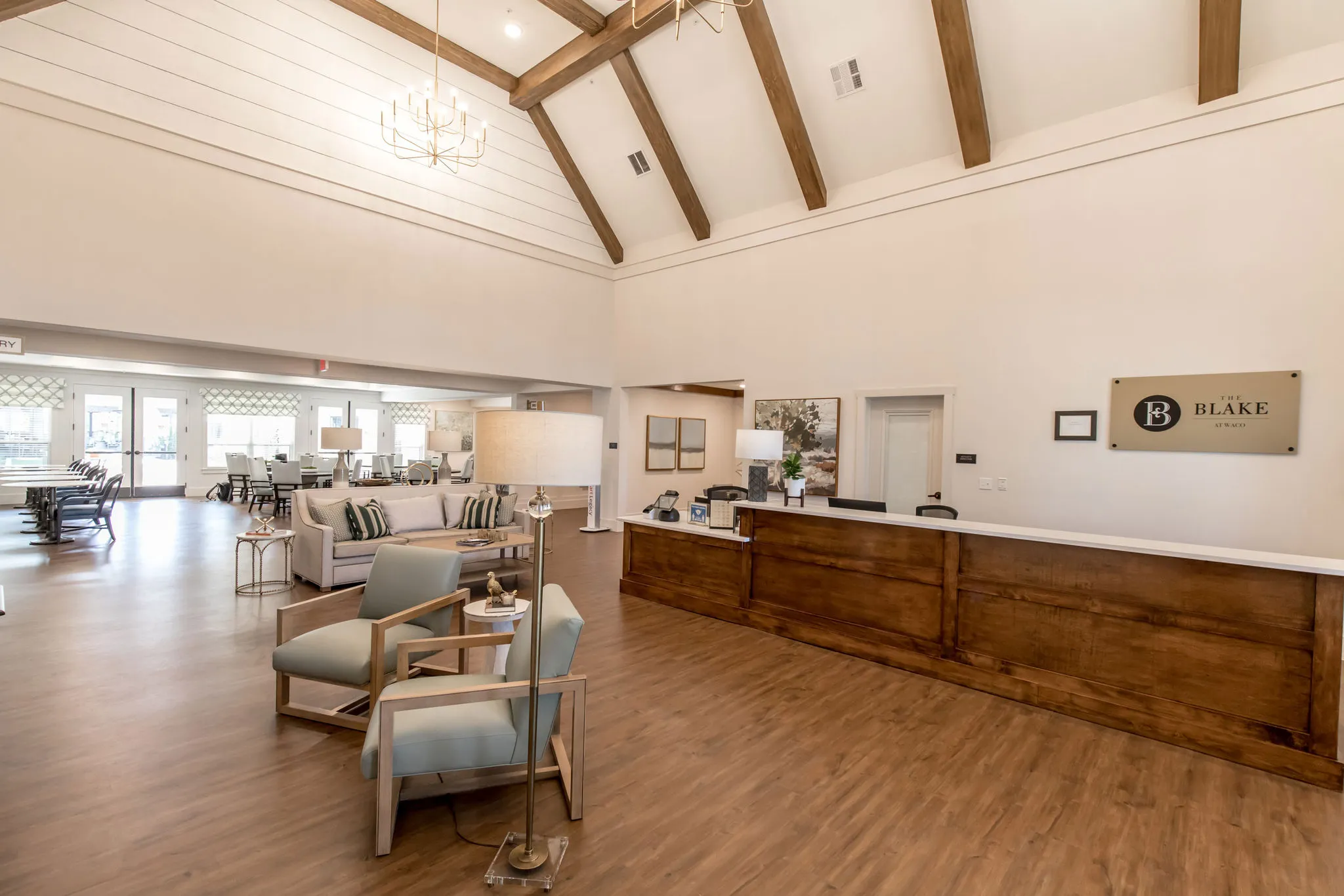 Senior living lobby with a walnut reception desk below the exposed timber trusses, the living room beyond