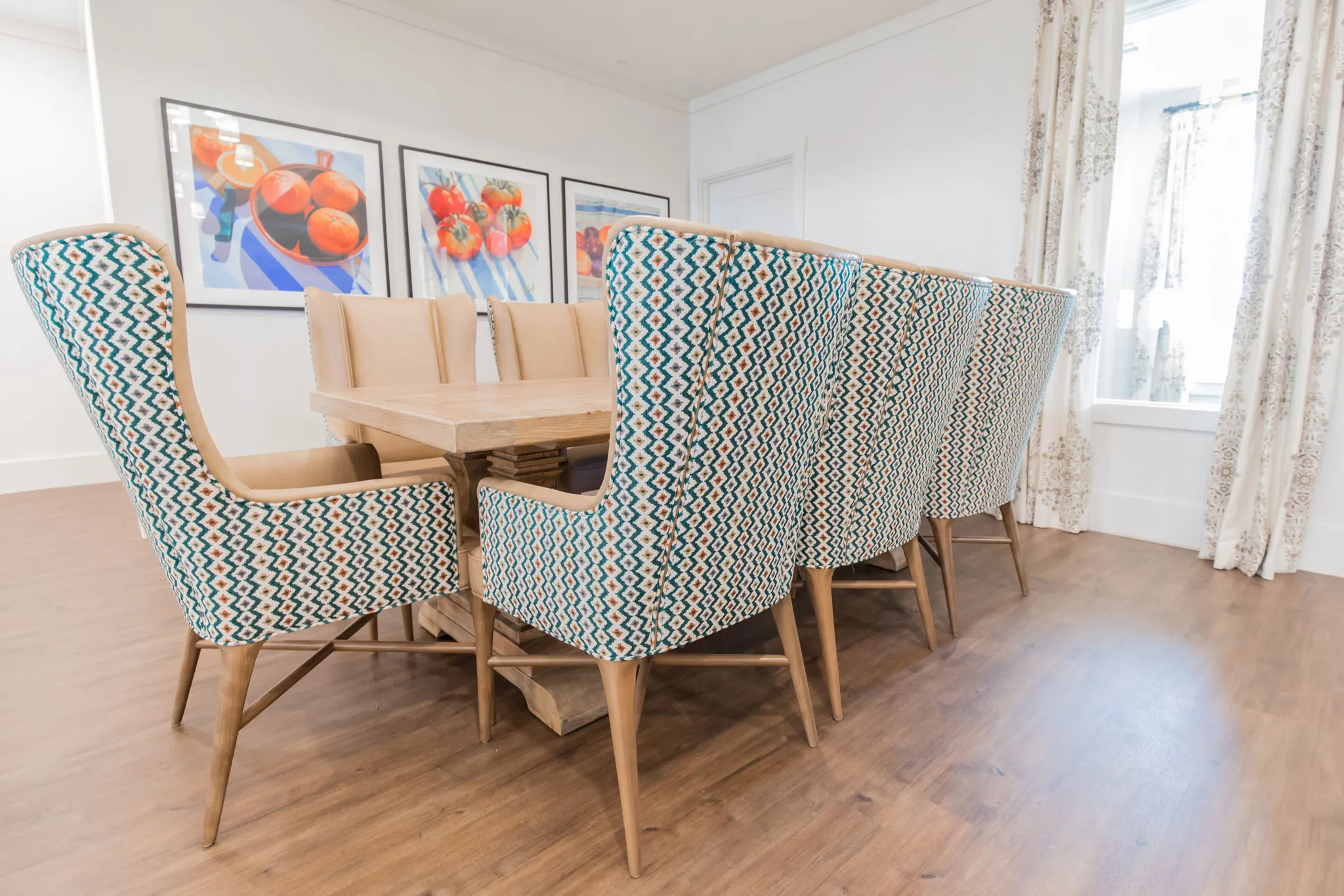 Senior living dining nook with teal chevron wing chairs at a light oak table below framed still lifes