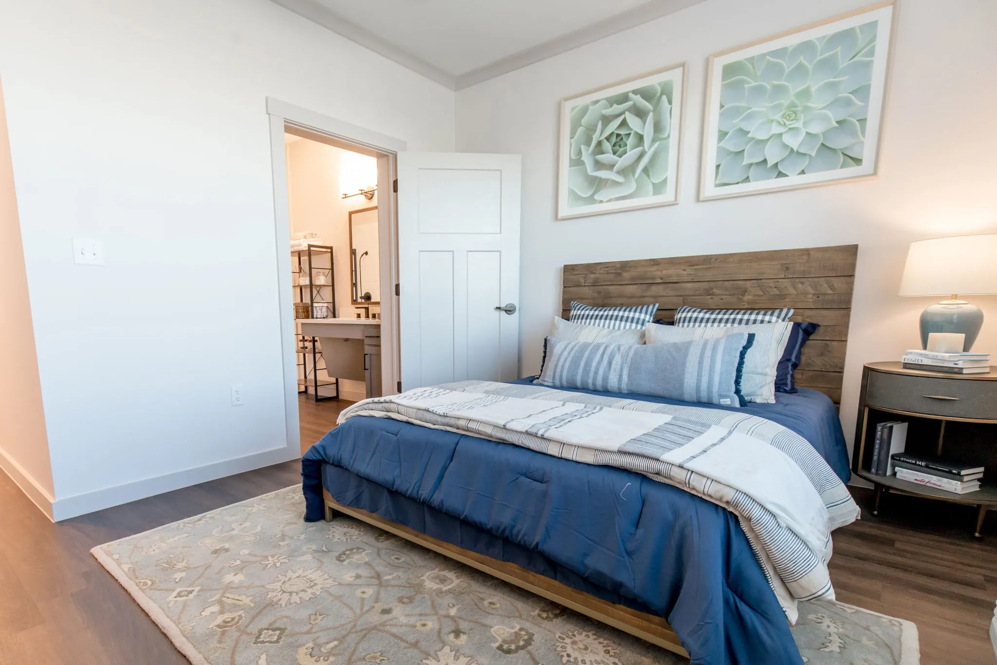 Senior living model bedroom with a plank headboard and layered blue bedding, succulent prints above