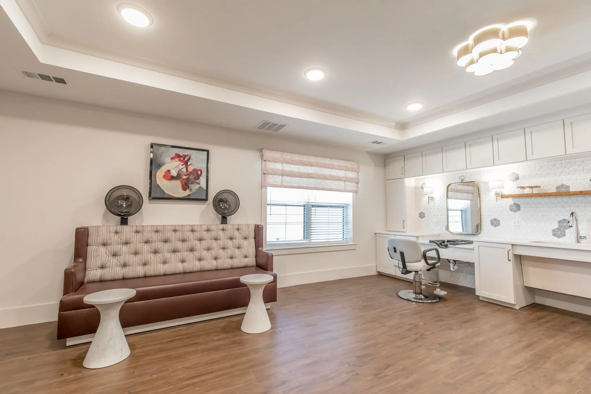 Senior living salon with a tufted burgundy banquette below wall-mounted hood dryers, a styling chair and washbowl beyond