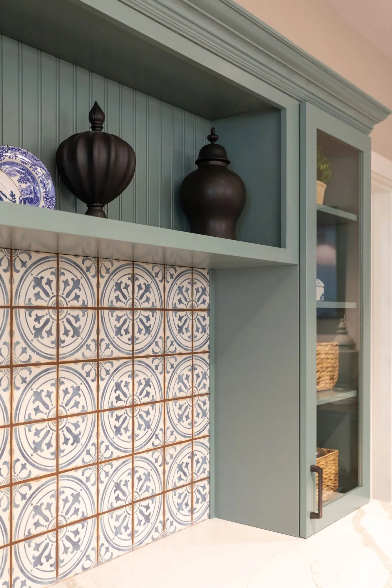 Senior living interior detail: blue and white patterned tile beneath sage open shelving holding black lidded urns