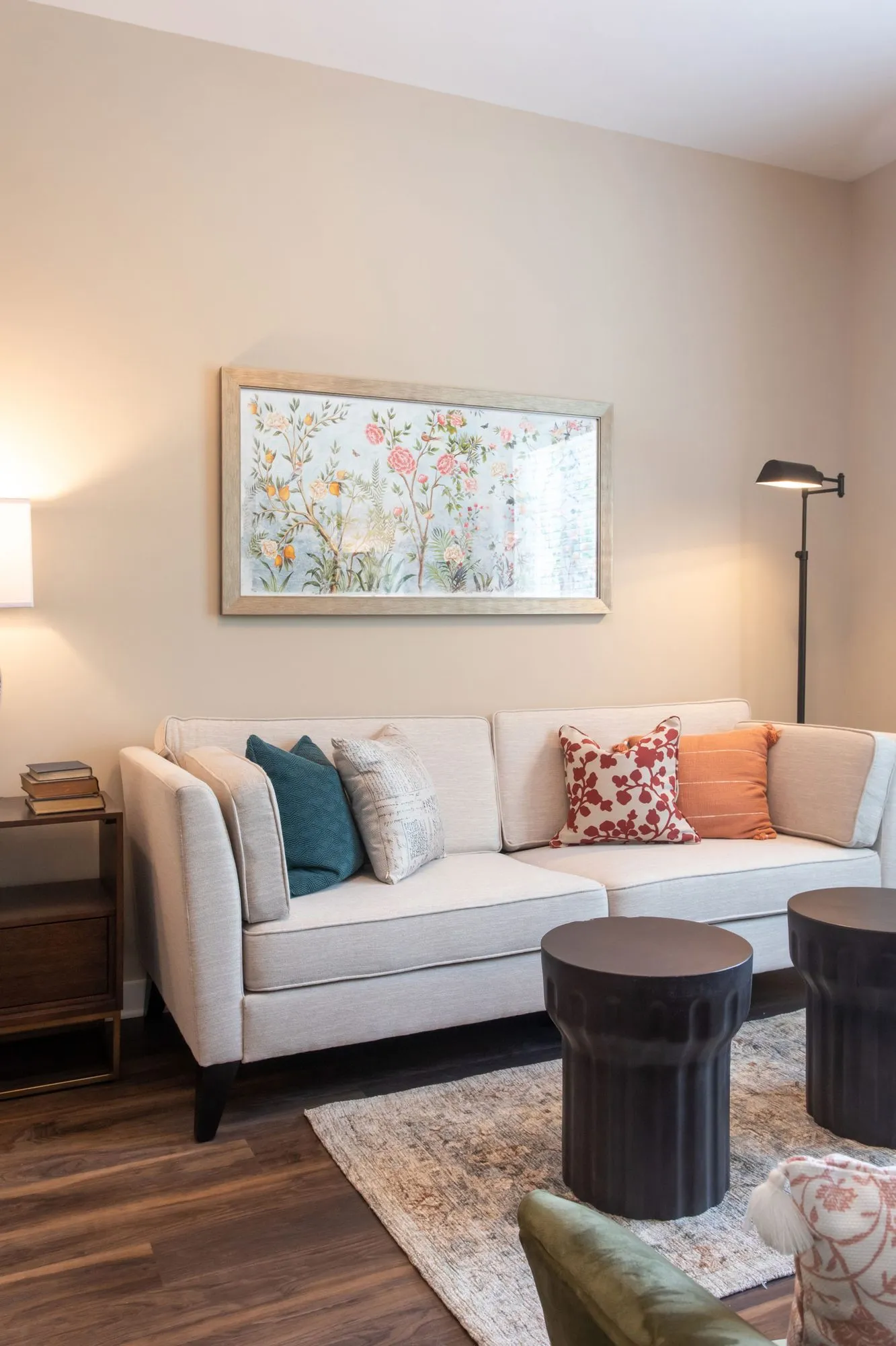 Senior living living room with a cream sofa and patterned pillows, dark drum tables and a botanical print above