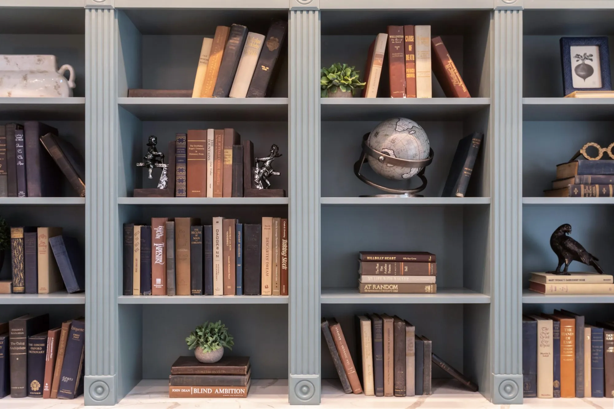 Senior living interior detail: blue-grey bookcases with fluted pilasters holding old books, a globe and black bird figures