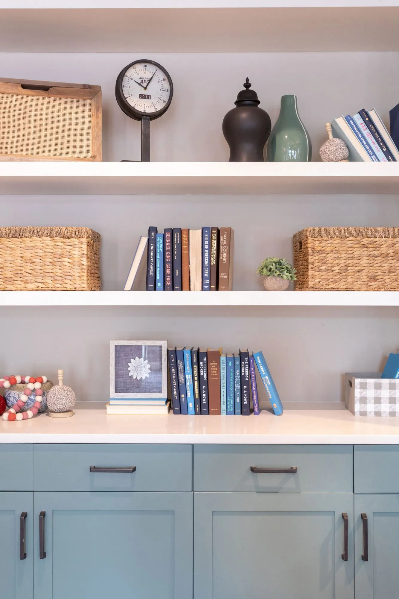 Senior living interior detail: white open shelves with books, baskets, a clock and vases above sage lower cabinets