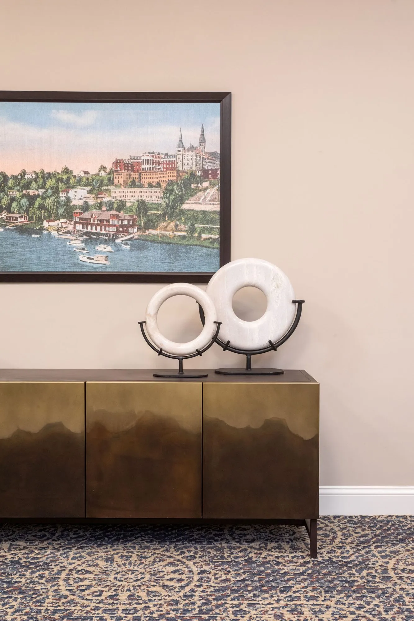 Senior living interior detail: bronze-finish sideboard with white stone ring sculptures below a painted harbour cityscape