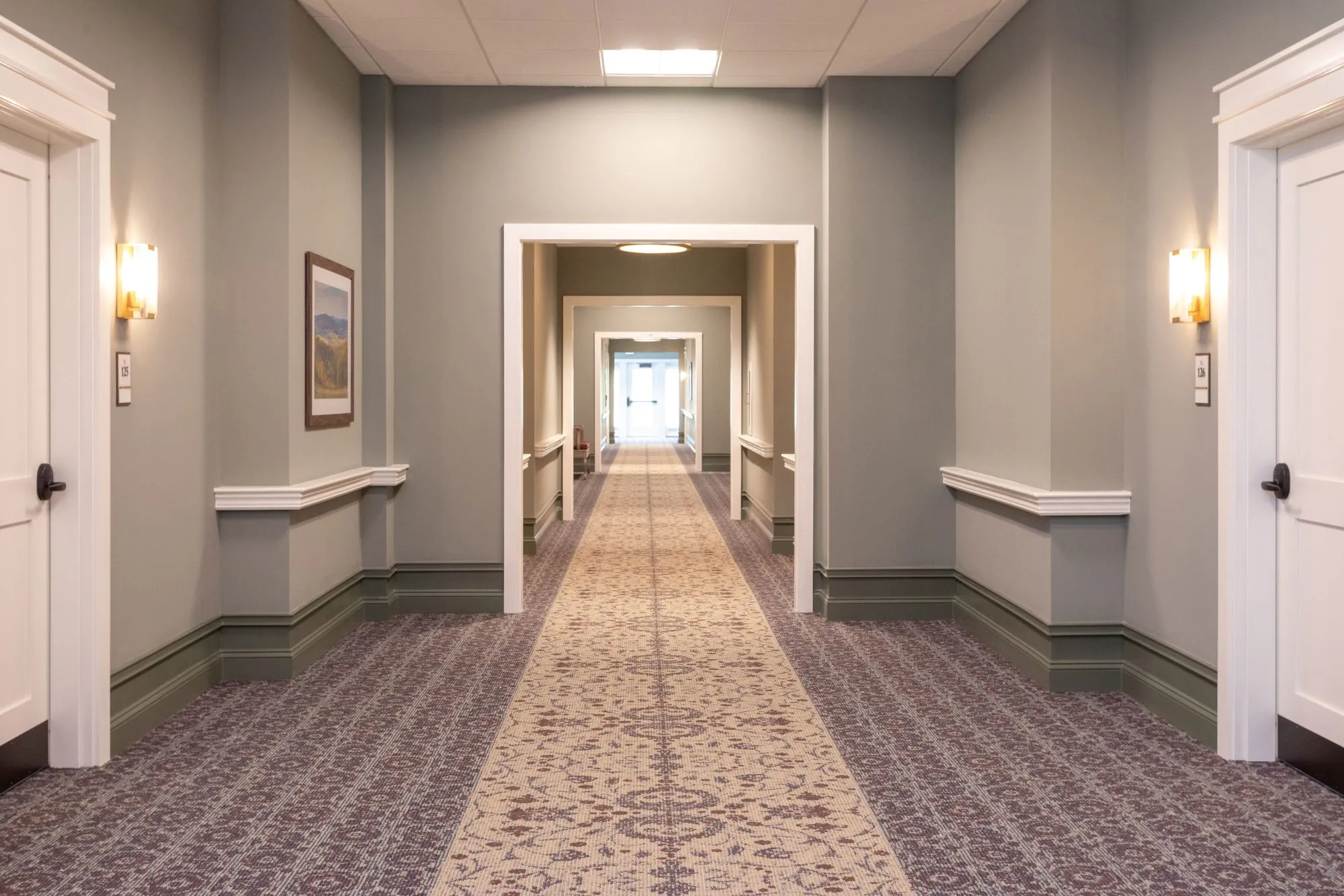 Senior living residential corridor with a patterned runner, grey walls with a handrail and white door casings