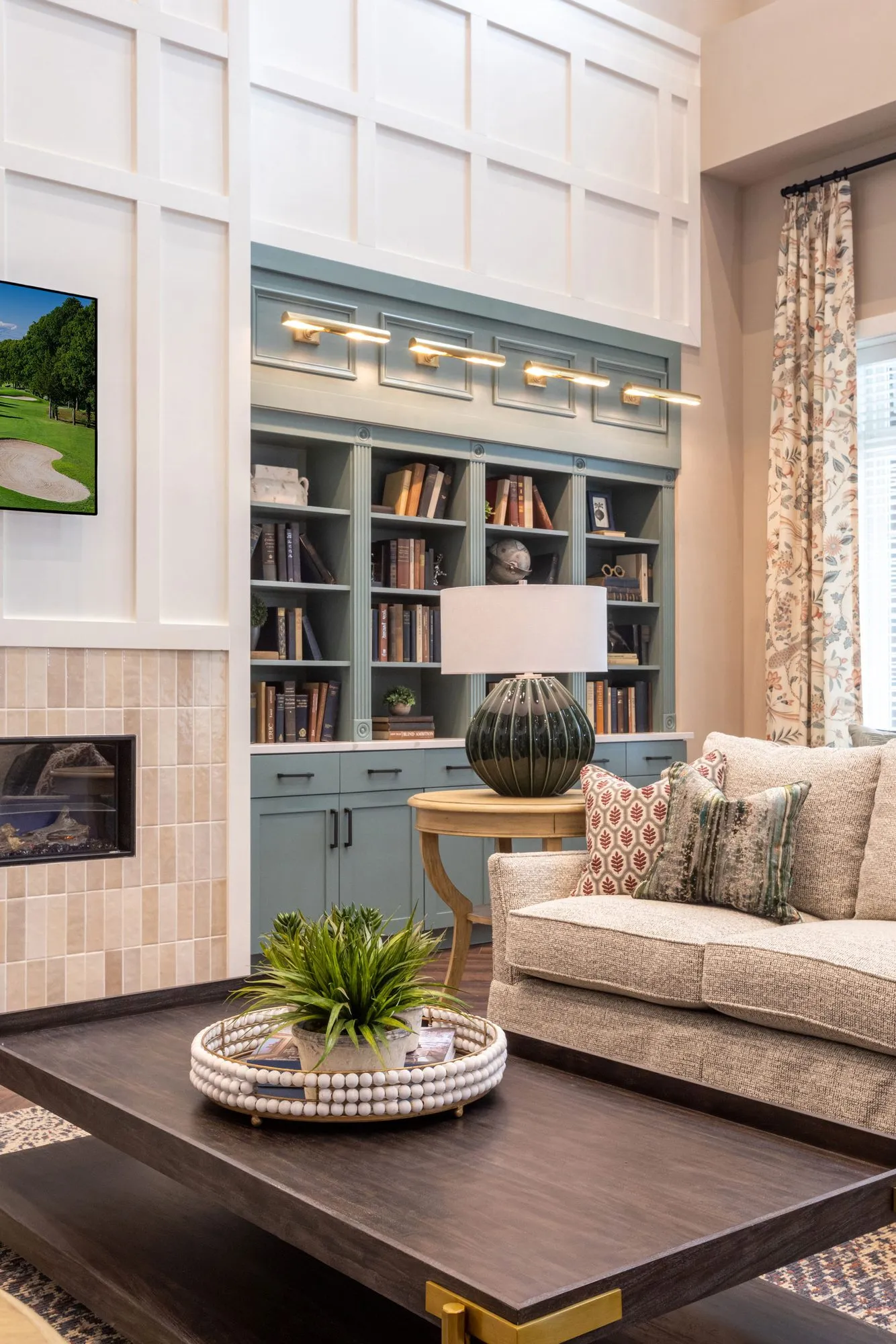 Senior living living room with a linen sofa and dark coffee table before sage bookcases and a tiled fireplace