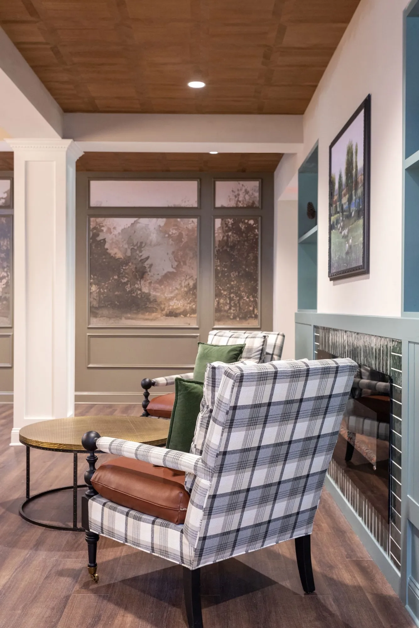 Senior living interior detail: plaid wing chair with a leather bolster beside a sage beadboard wall under a coffered ceiling