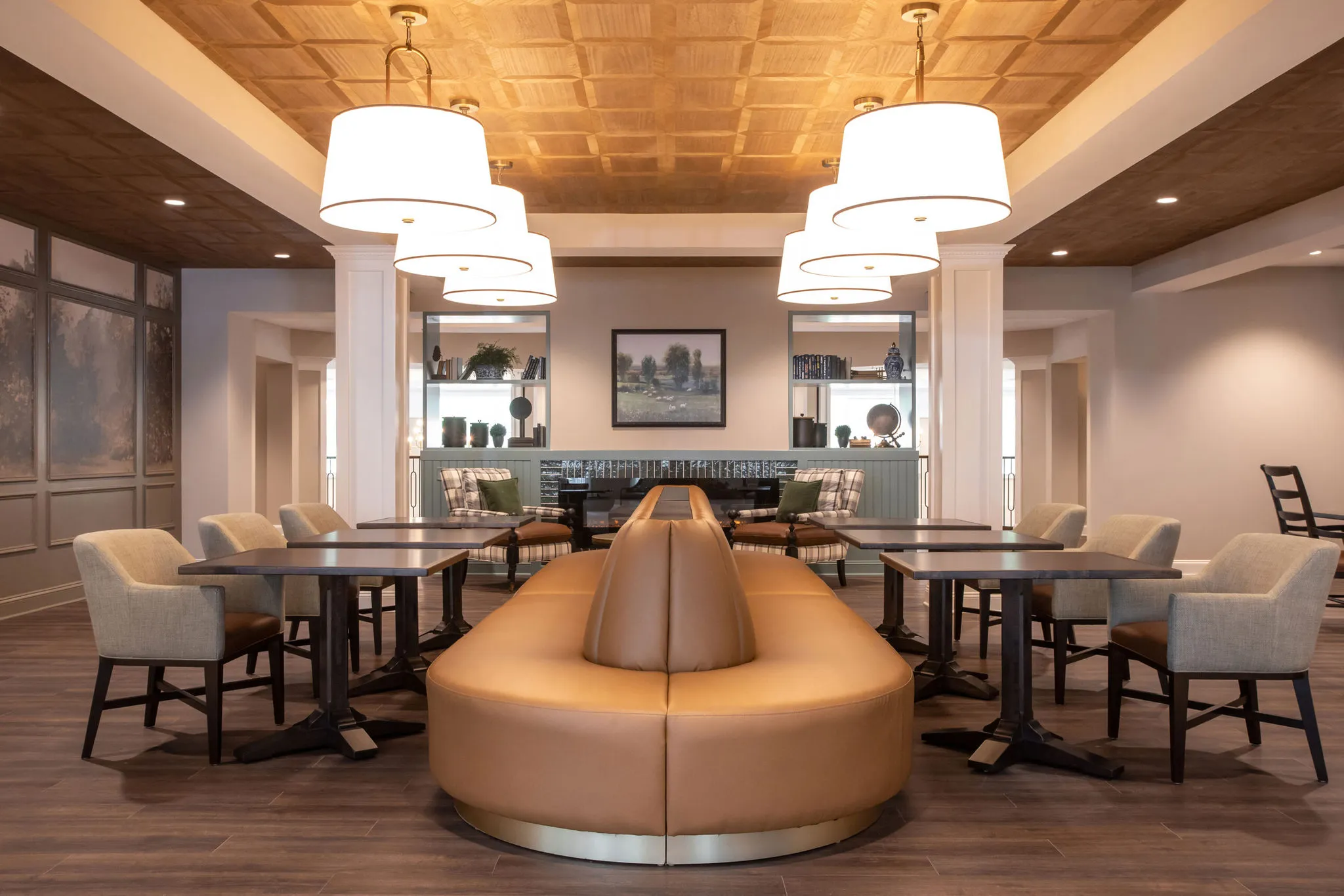 Senior living bistro with a curved leather banquette between cafe tables under drum pendants and a coffered wood ceiling