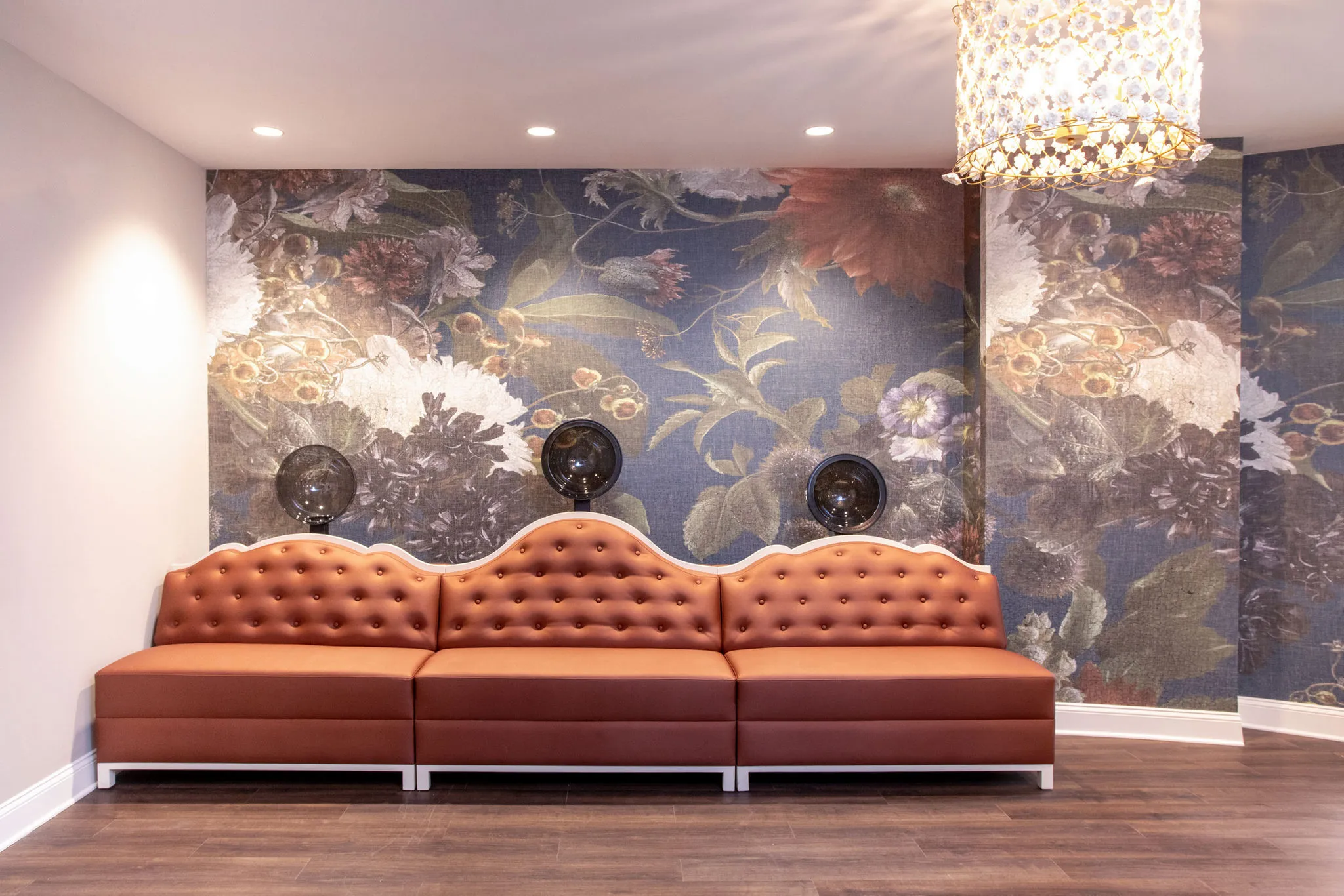 Senior living lounge with a terracotta tufted banquette against a floor-to-ceiling floral mural under a crystal chandelier