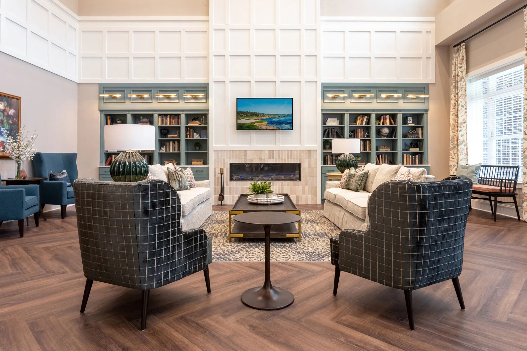 Senior living living room with a gas fireplace between sage bookcases and windowpane wing chairs on a patterned rug