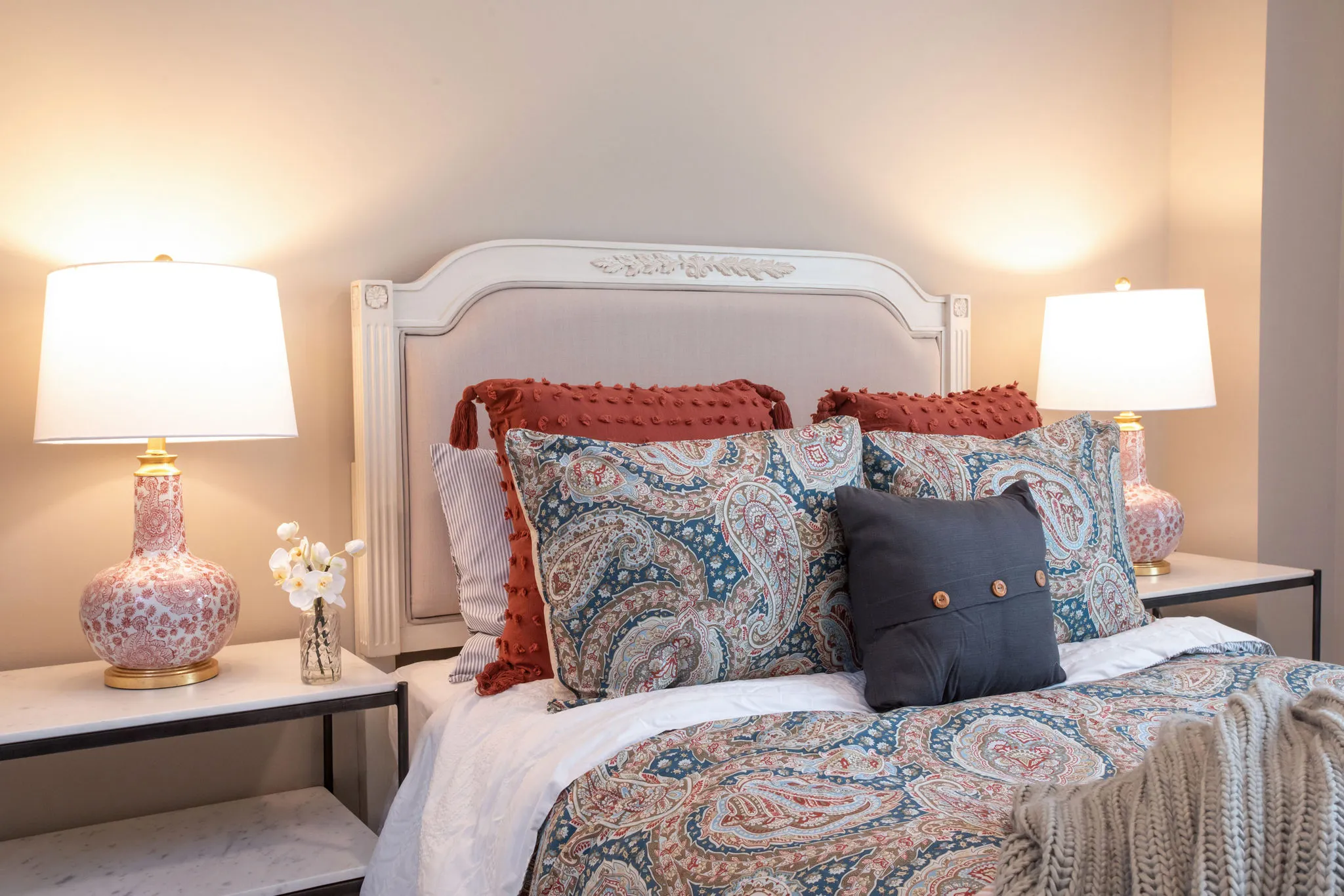 Senior living model bedroom with paisley bedding and rust shams on a carved headboard between lamp-lit nightstands