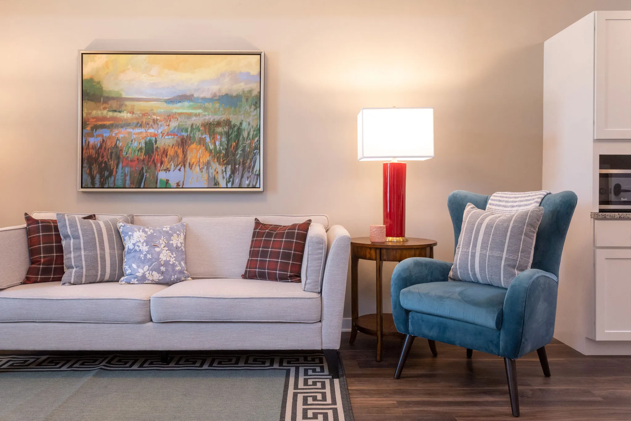 Senior living model living room with a teal wing chair beside a linen sofa under a marsh landscape painting