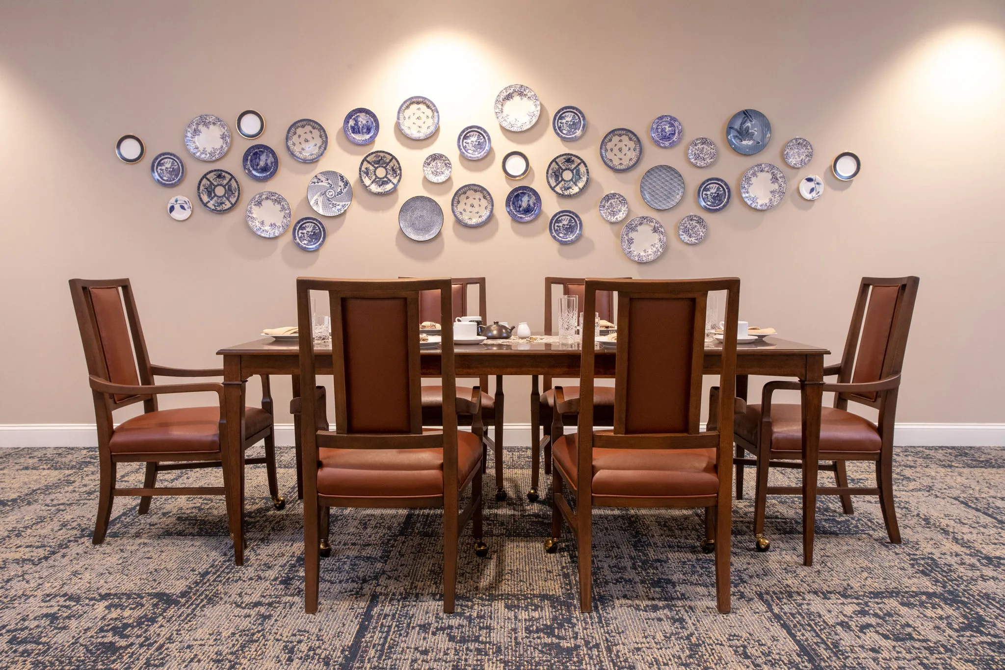 Senior living private dining room with a walnut table and leather chairs beneath a wall of blue and white transferware plates