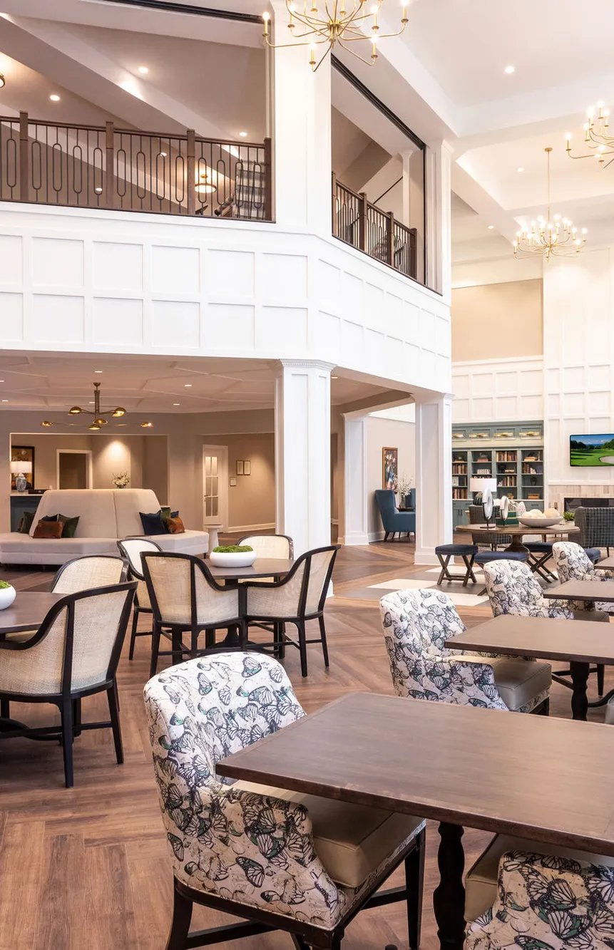 Senior living two storey dining room with white panelling and brass chandeliers, interior design by Banko Design at Cadence At Olney, Olney, Maryland