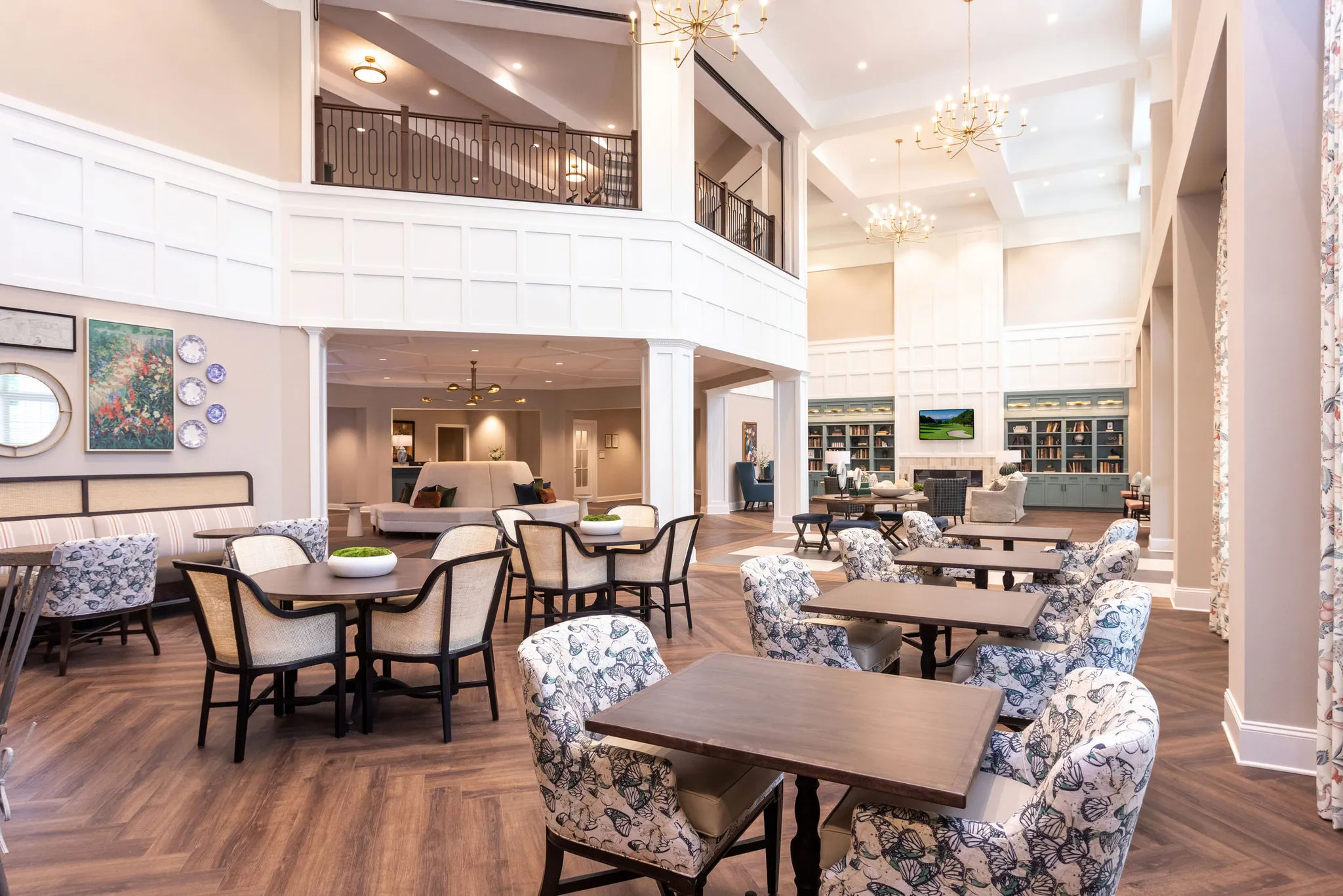Senior living two storey dining room with white panelling, a balcony rail, brass chandeliers and butterfly print armchairs