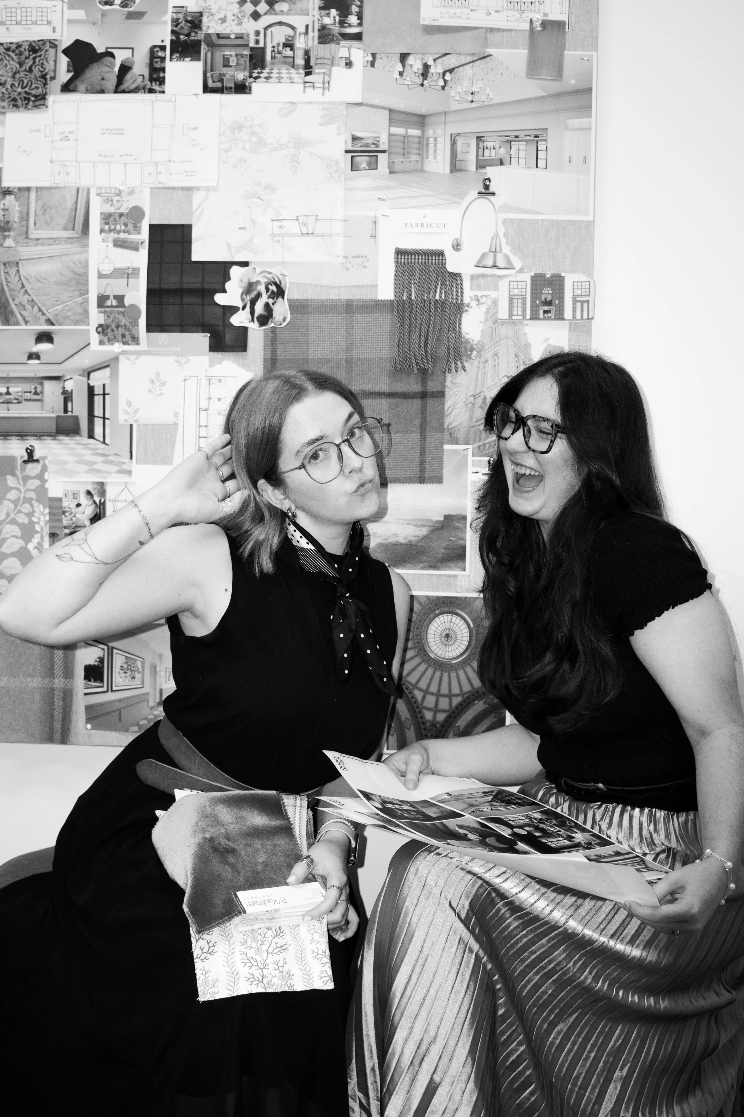 Two Banko Design designers clowning in front of a pin board of interior photographs, one holding fabric samples, the other a magazine