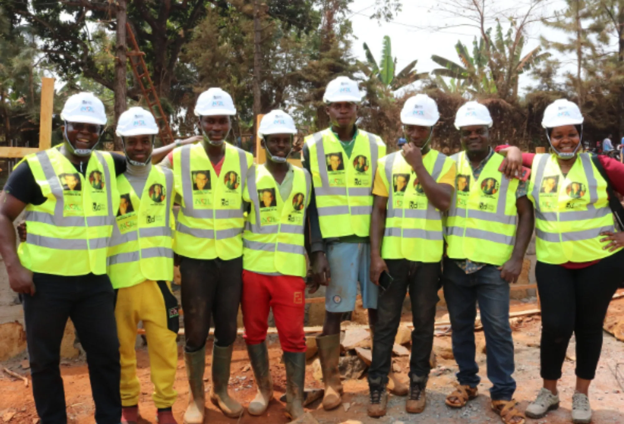 Nine workers in yellow high-visibility vests and white hard hats standing together on a school building site in Cameroon