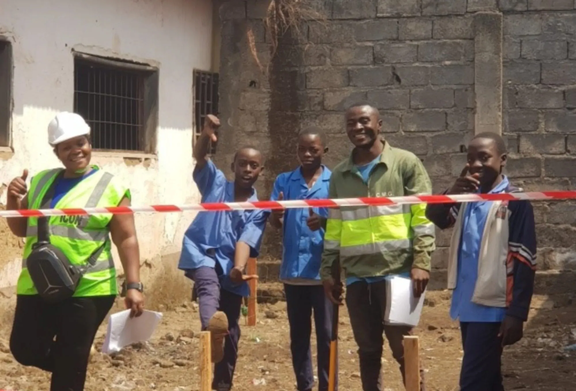 A site supervisor, schoolchildren in blue uniforms and a worker behind barrier tape at a new block-built sanitation building