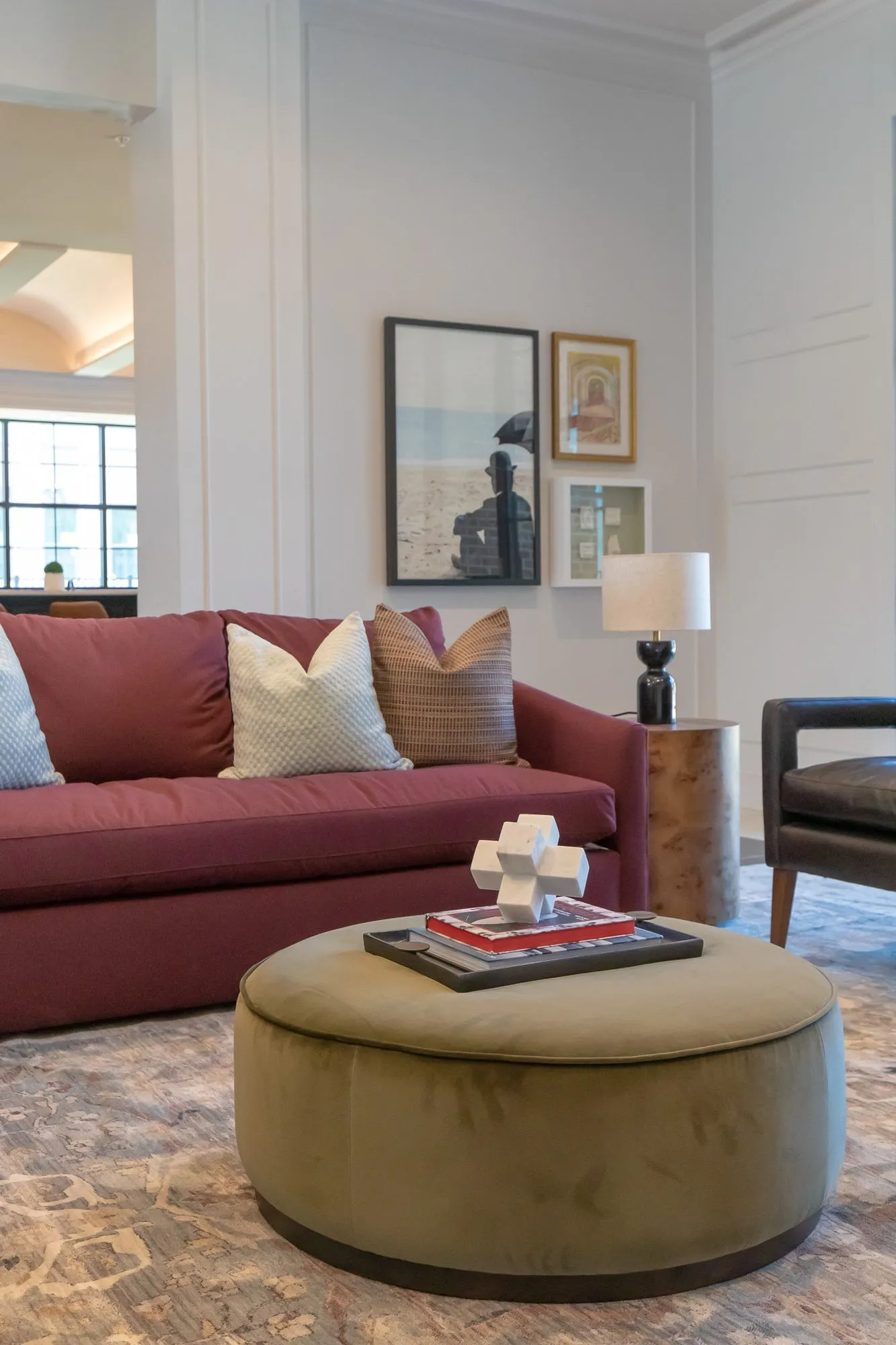 Multifamily amenity clubroom with a burgundy sofa and olive velvet ottoman, interior design by Banko Design at Chastain Hill, Douglasville, Georgia