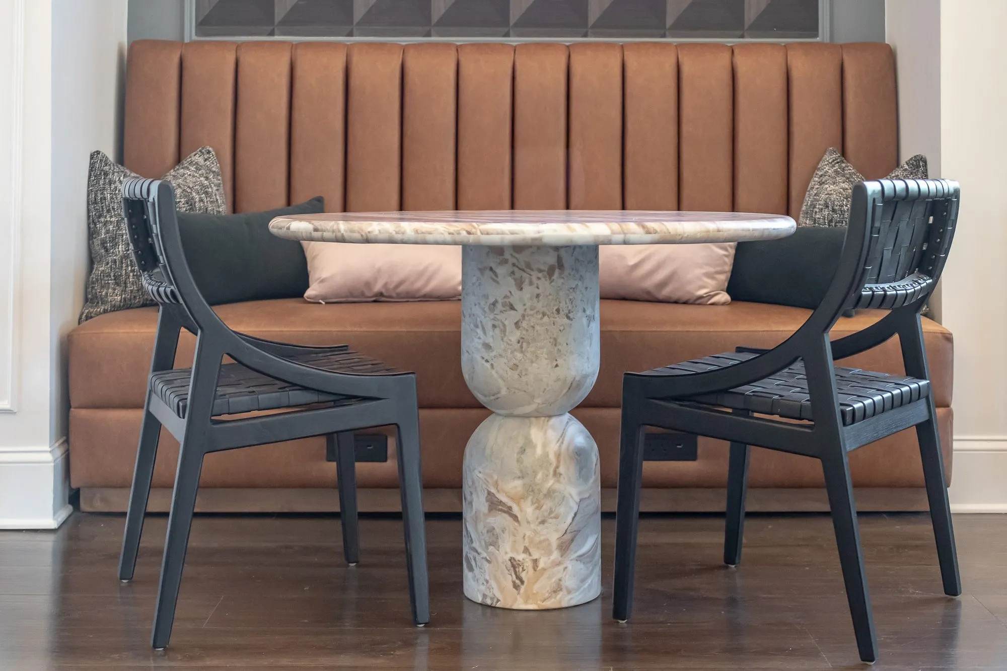 Multifamily amenity interior detail: cognac channel-tufted banquette with a marble pedestal table and woven leather chairs