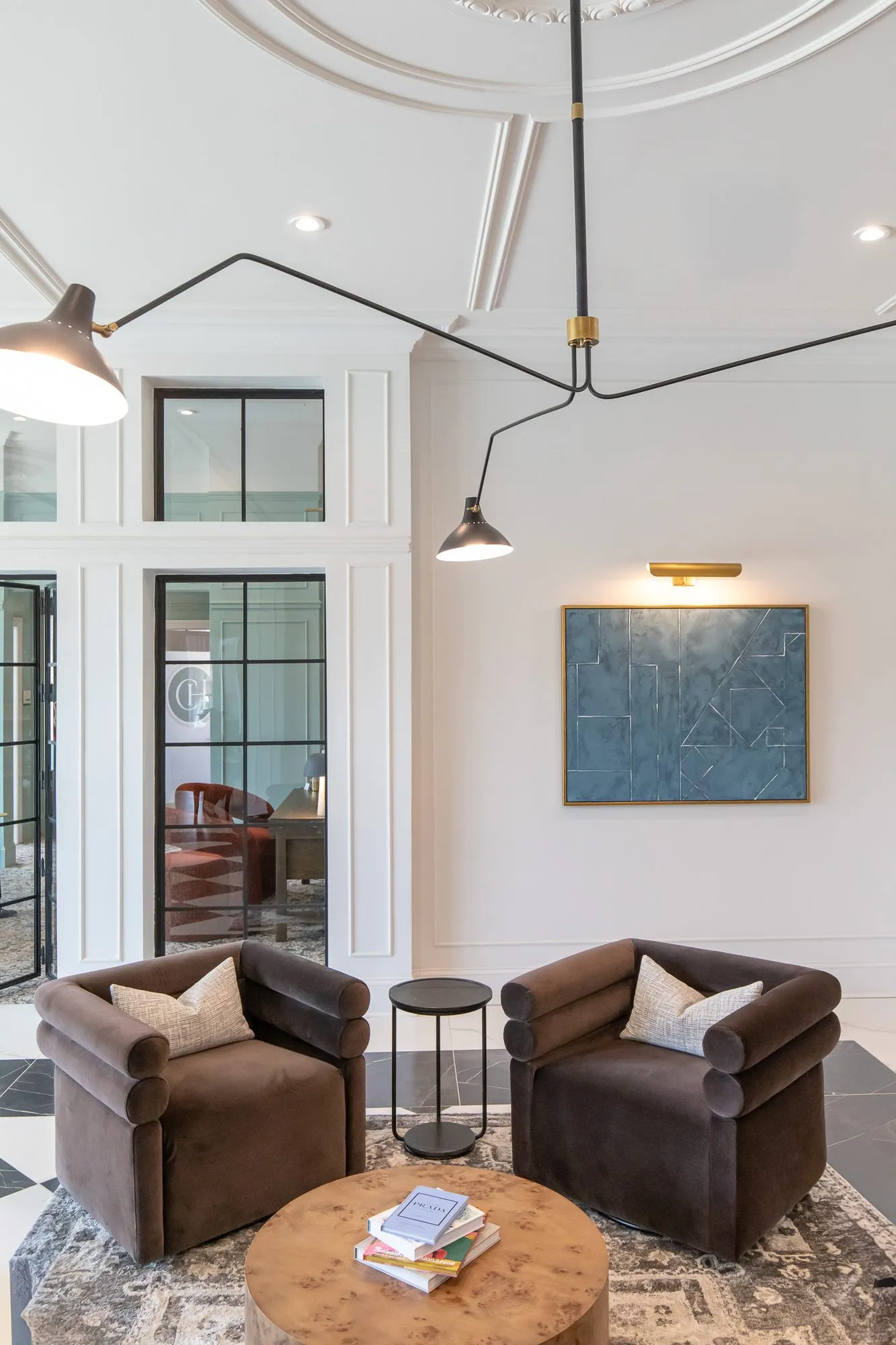 Multifamily amenity lobby lounge with two brown velvet barrel chairs at a burl table under a black multi-arm ceiling light