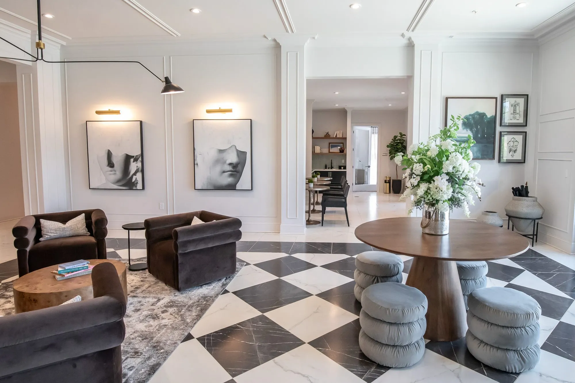 Multifamily amenity lobby with brown velvet chairs and a flower-topped round table on checkerboard marble, framed face prints